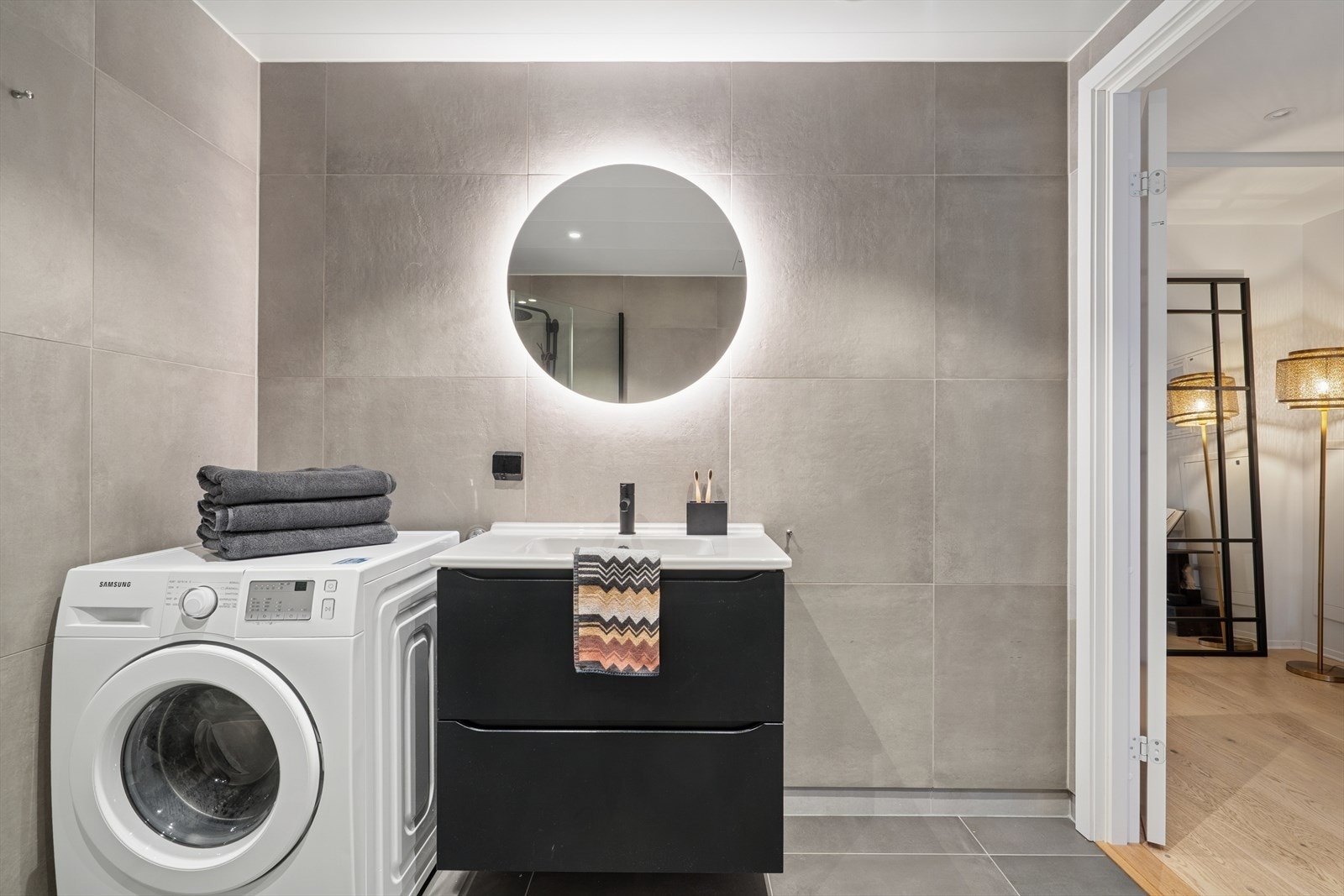 Innredningen består av en heldekkende servant med ett-greps blandebatteri, vegghengt speil med belysning og vegghengt toalett. Videre er det dusjhjørne med glassdører og praktisk opplegg for vaskemaskin. Galleribilde