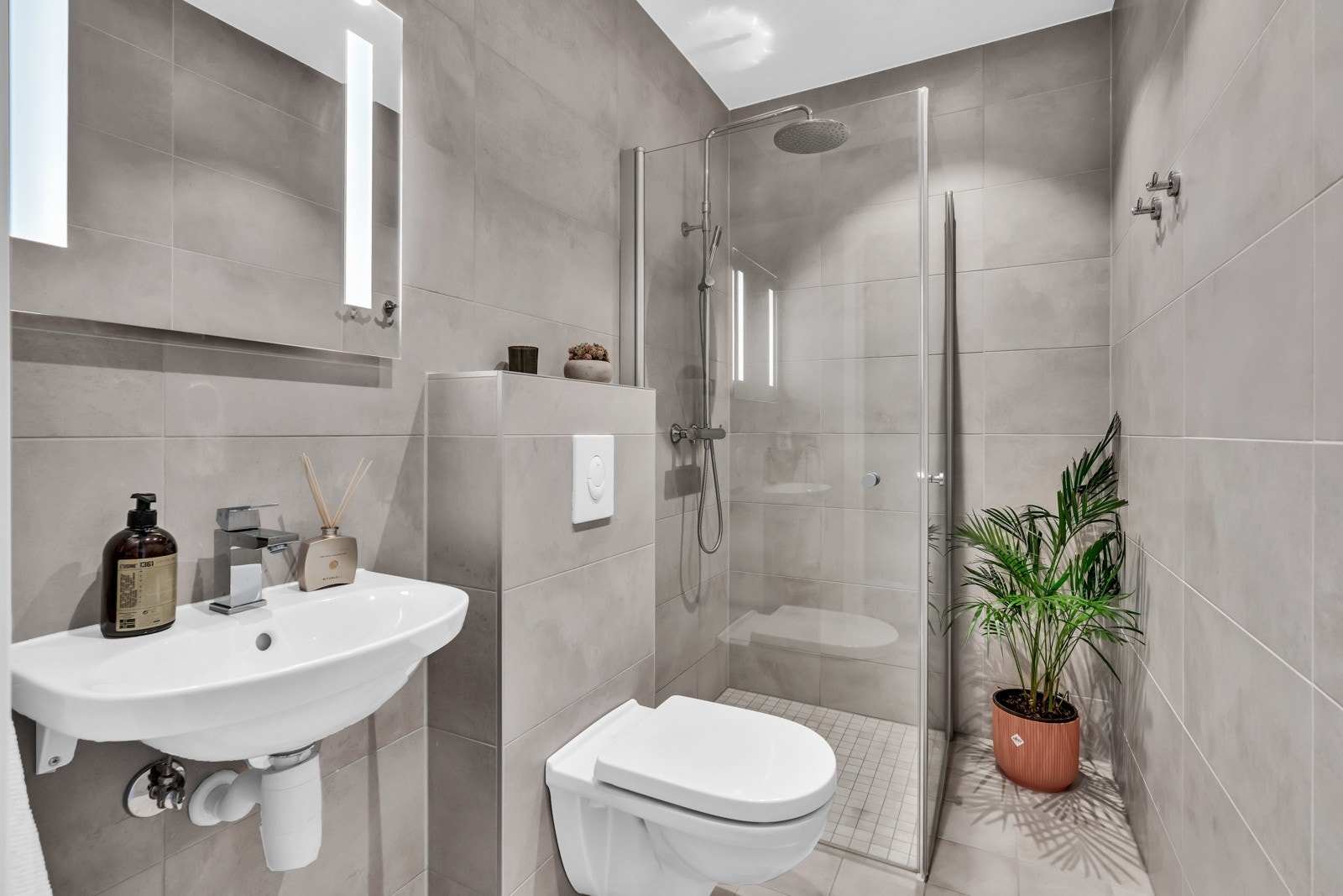 Baderommet har servant, veggmontert toalett og dusjvegger/hjørne med regnfall. Galleribilde