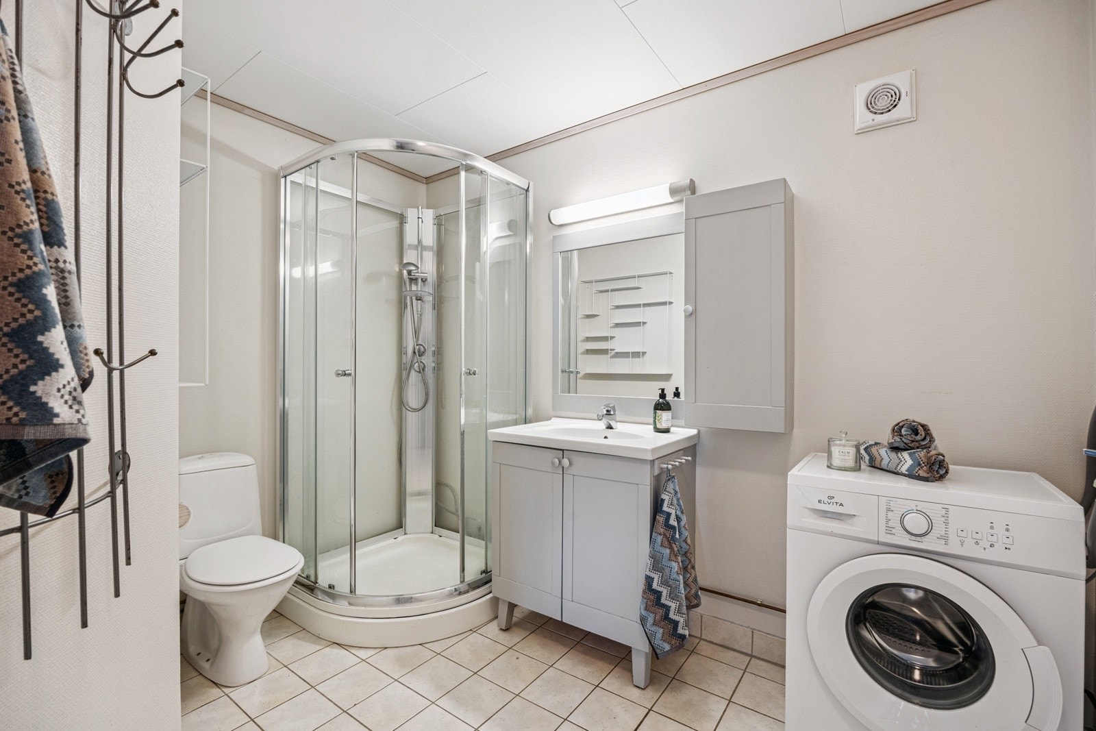 Badet er innredet med fliser, dusjkabinett, toalett, veggspeil og servant. Galleribilde