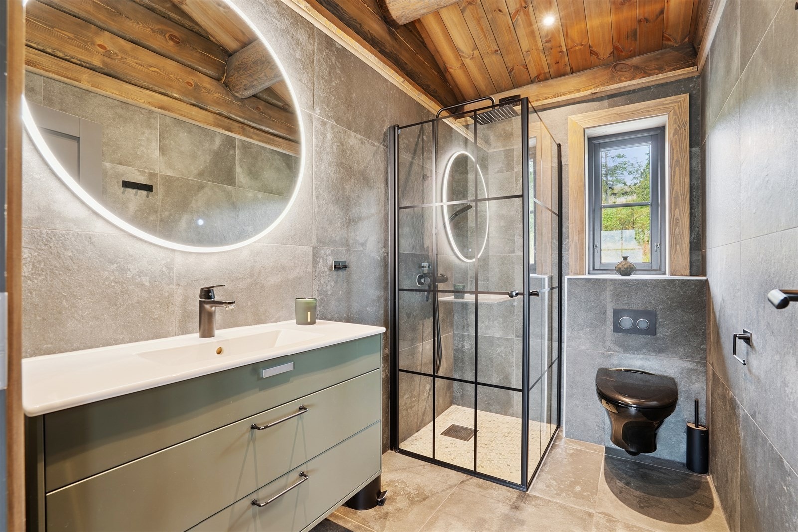 Flislagt baderom ved kjøkken med gulvvarme og downlights, og utstyrt med nedfelt servant i baderomsinnredning, vegghengt toalett og regnfallsdusj i dusjhjørne med dusjvegger. Galleribilde