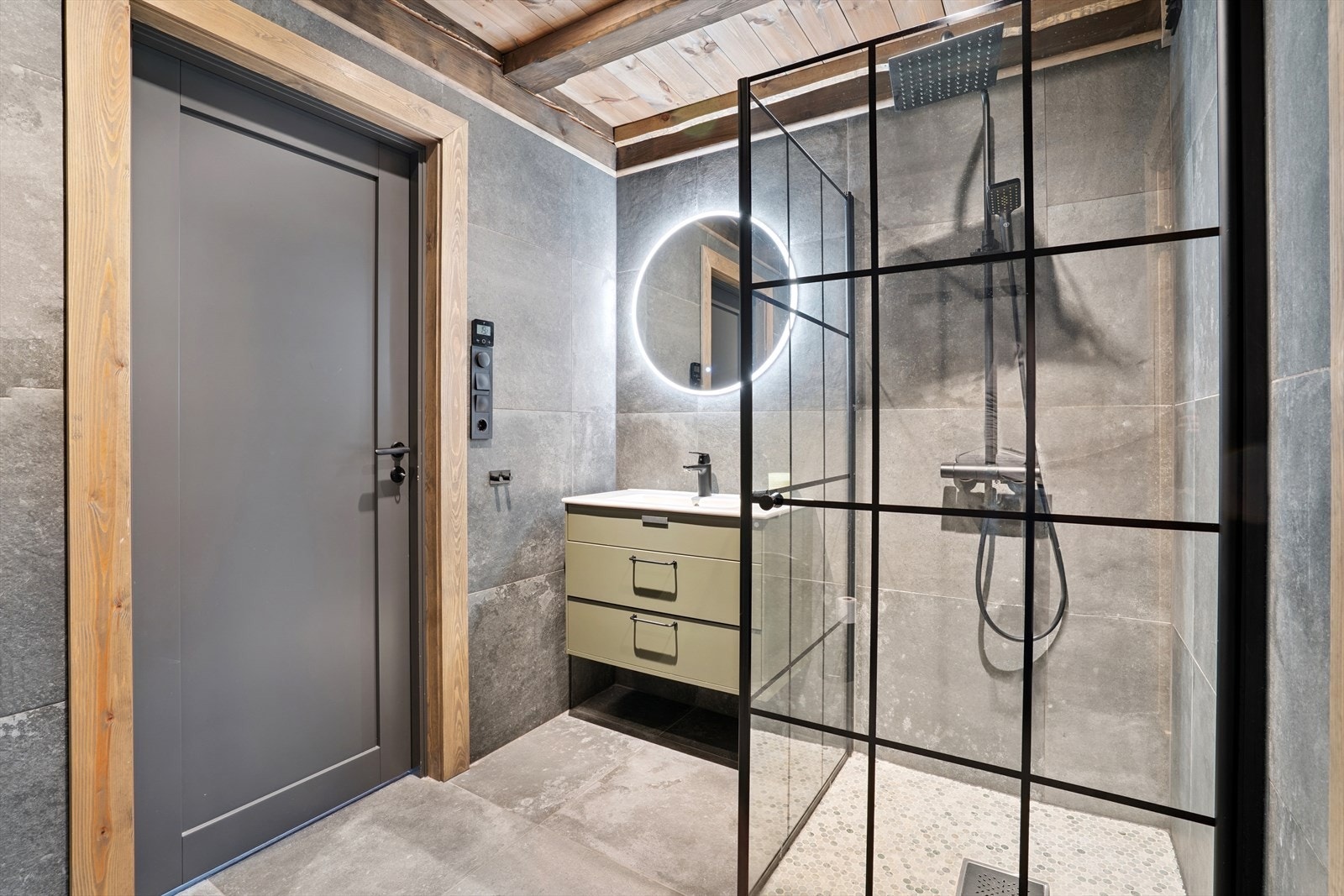 Badet er utstyrt med en grå glatt innredning med nedfelt servant i baderomsinnredning, vegghengt toalett og regnfallsdusj i dusjhjørne med dusjvegger. Galleribilde