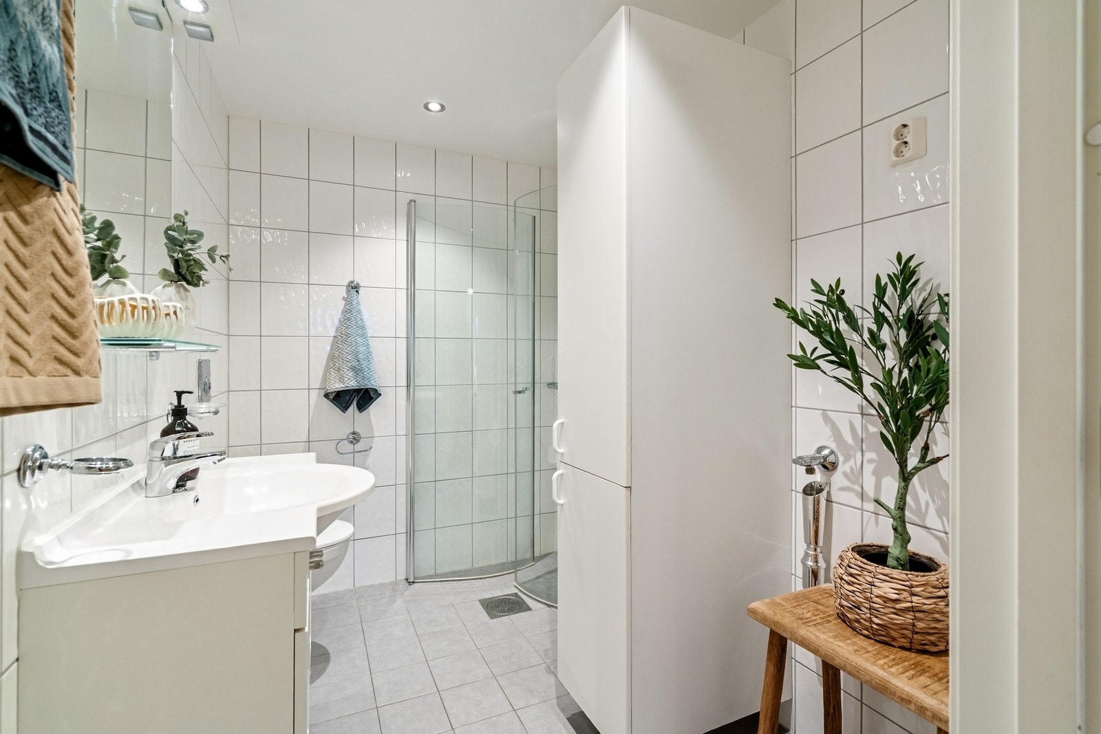 Bad/vaskerommet er også flislagt med varmekabler i gulv og har opplegg for vaskemaskin og tørketrommel. Rommet er utstyrt med servant, speil, veggmontert toalett og dusjhjørne. Galleribilde