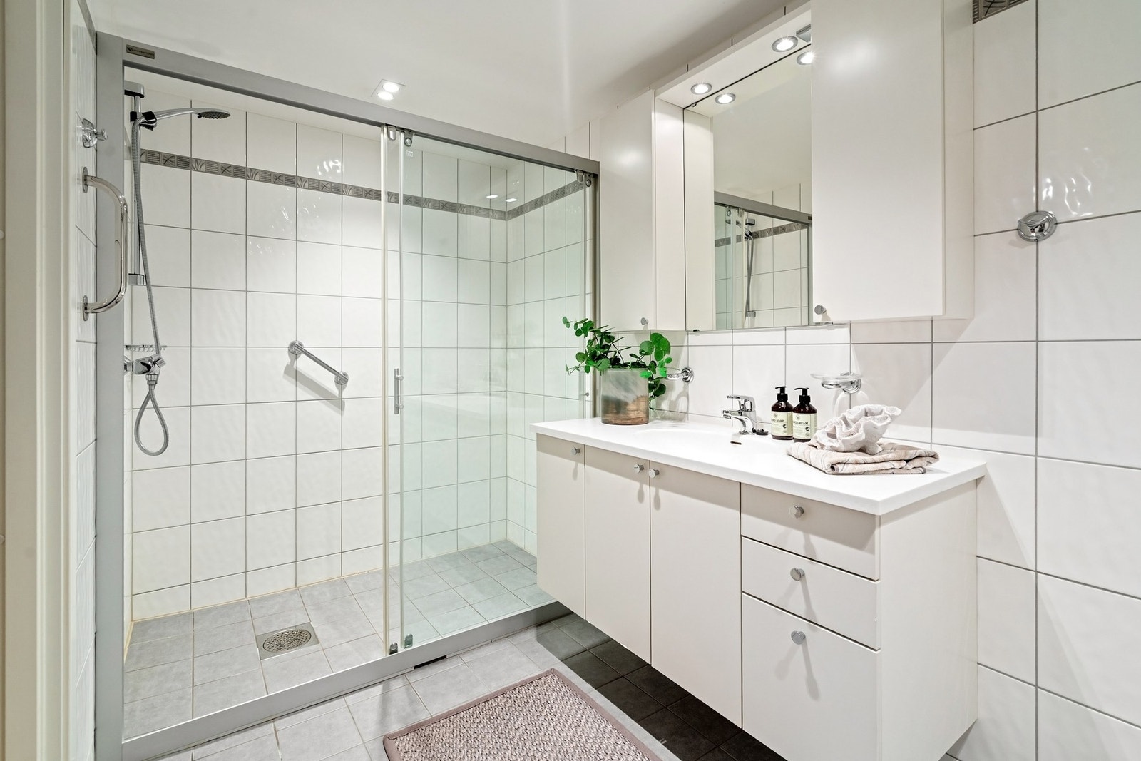 Badet er innredet med servantinnredning med heldekkende topplate, speil med belysning, veggmontert toalett og dusj med glassdører. Galleribilde