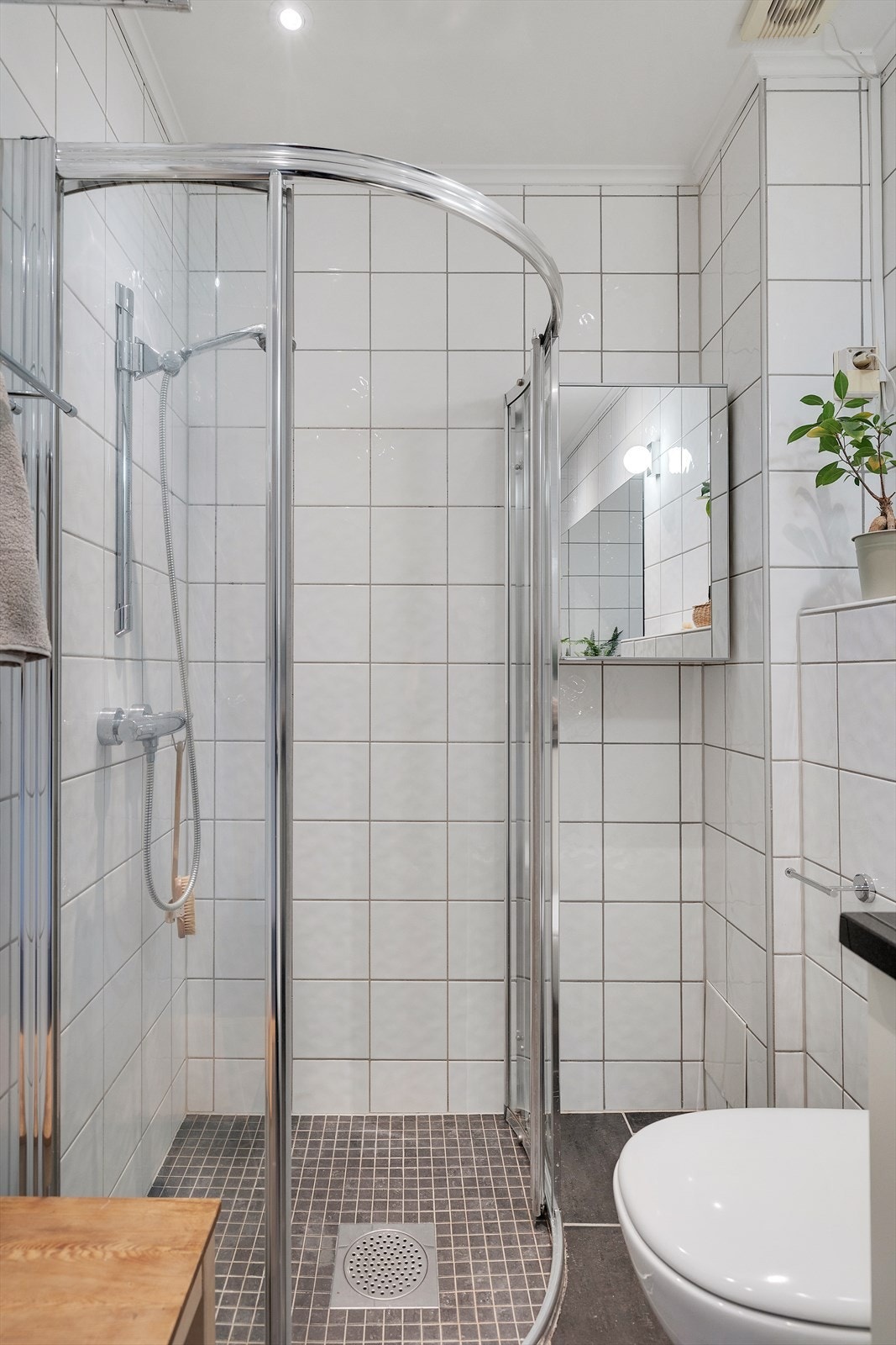 Videre er badet innredet med dusjhjørne med skyvedører av glass og dusjarmatur tilkoblet hånddusj samt vegghengt toalett. Galleribilde