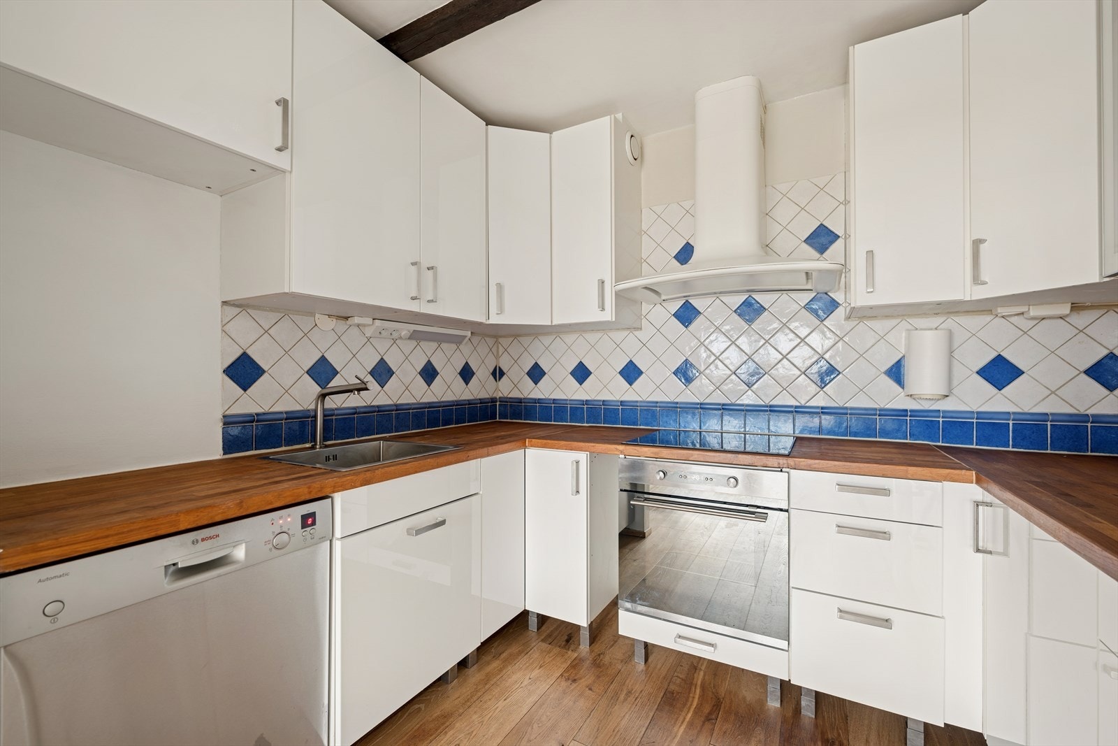 Kjøkkenet består av glatte høyglansfronter, benkeplate i tre og hvitevarer Galleribilde