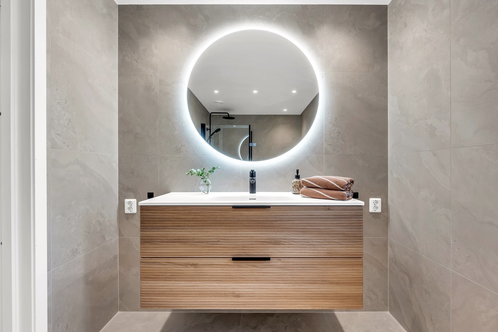 Badet er utstyrt med servant i baderomsinnredning, stor speile med belysning, veggmontert toalett og dusjhjørne med innfellbare dører Galleribilde