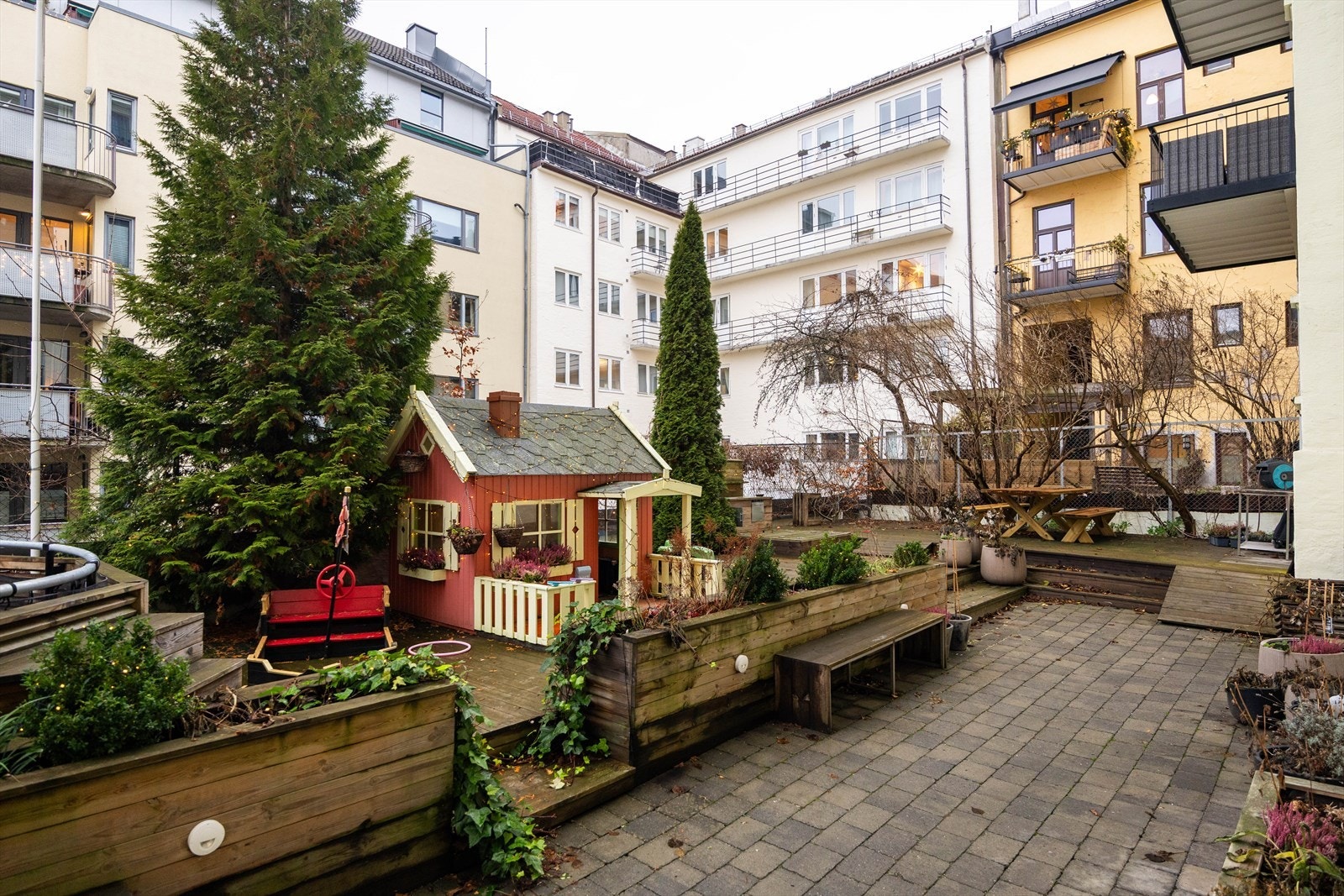 Meget pent opparbeidet og hellelagt gårdsrom med markterrasser, dukkestue og lekeapparater. Galleribilde