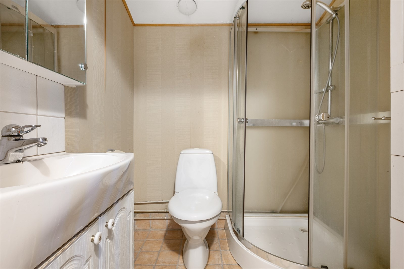 Badet i 1.etasje har fliser på gulv over gulvvarme. Innredet med helservant på skapseksjon, speilskap, klosett og dusjkabinett. Galleribilde