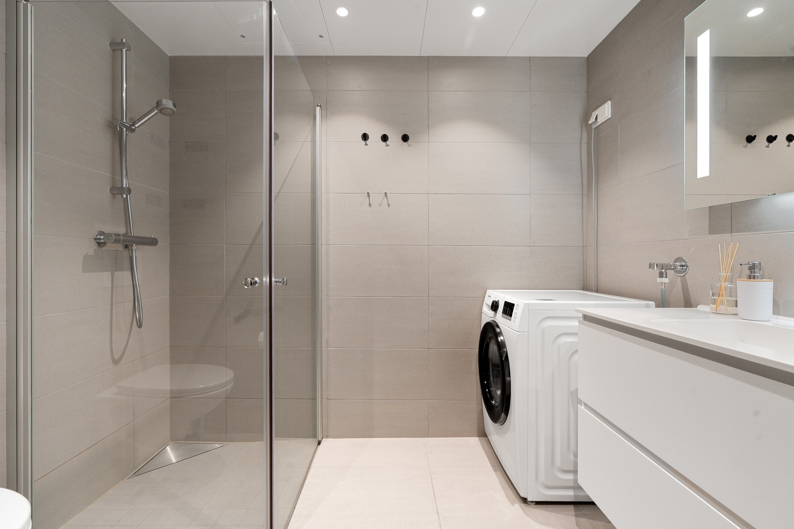 Delikat flislagt bad med vegghengt wc og baderomsinnredning og speil med belysning. Downlights i himling med dimming