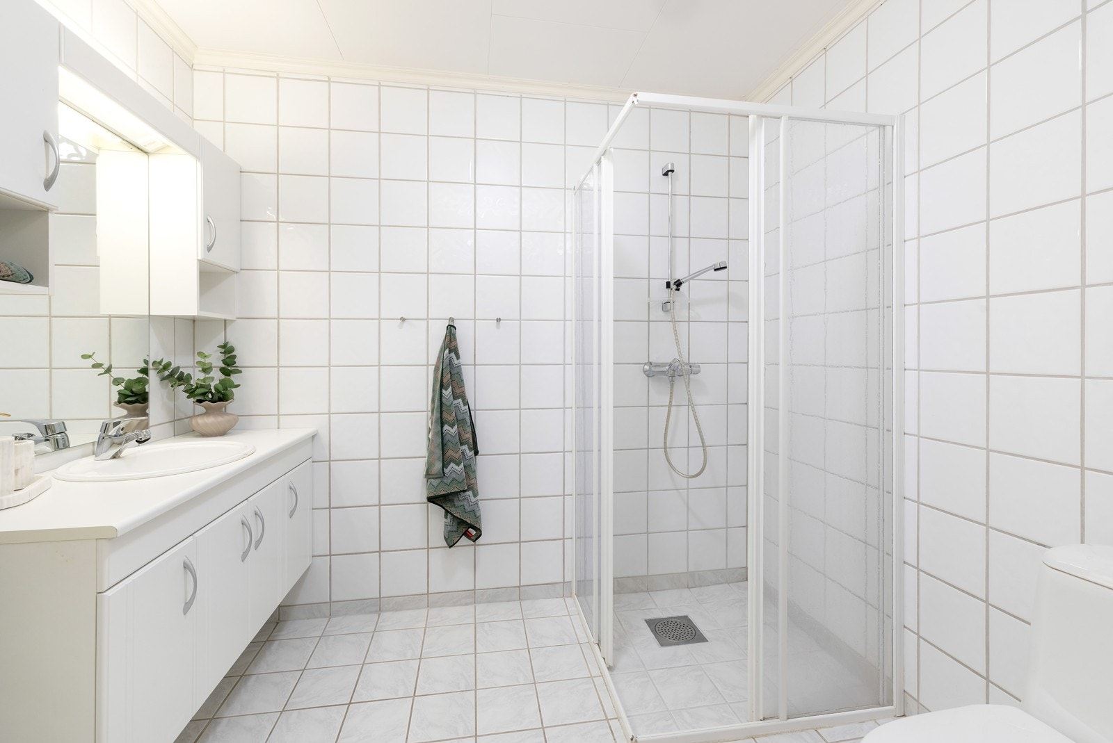 Flislagt bad innredet med wc, dusjhjørne og servant med skap. Galleribilde