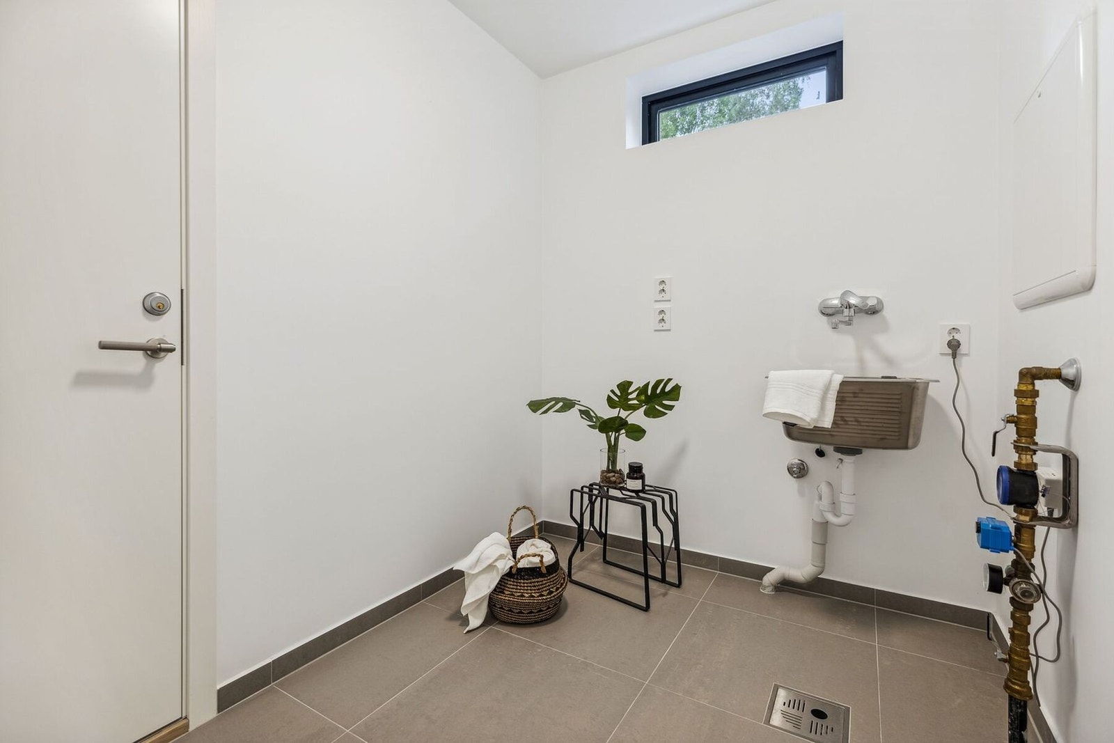 Praktisk vaskerom med fliser på gulv med gulvvarme og malte plater på vegg. Skyllekum i rustfritt stål og
opplegg for vaskemaskin. Galleribilde