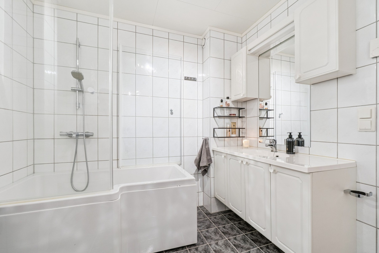 Boligens bad fremstår lyst og tidløst, og er utstyrt med servant med under- og overskap, toalett og badekar med dusjløsning. Galleribilde