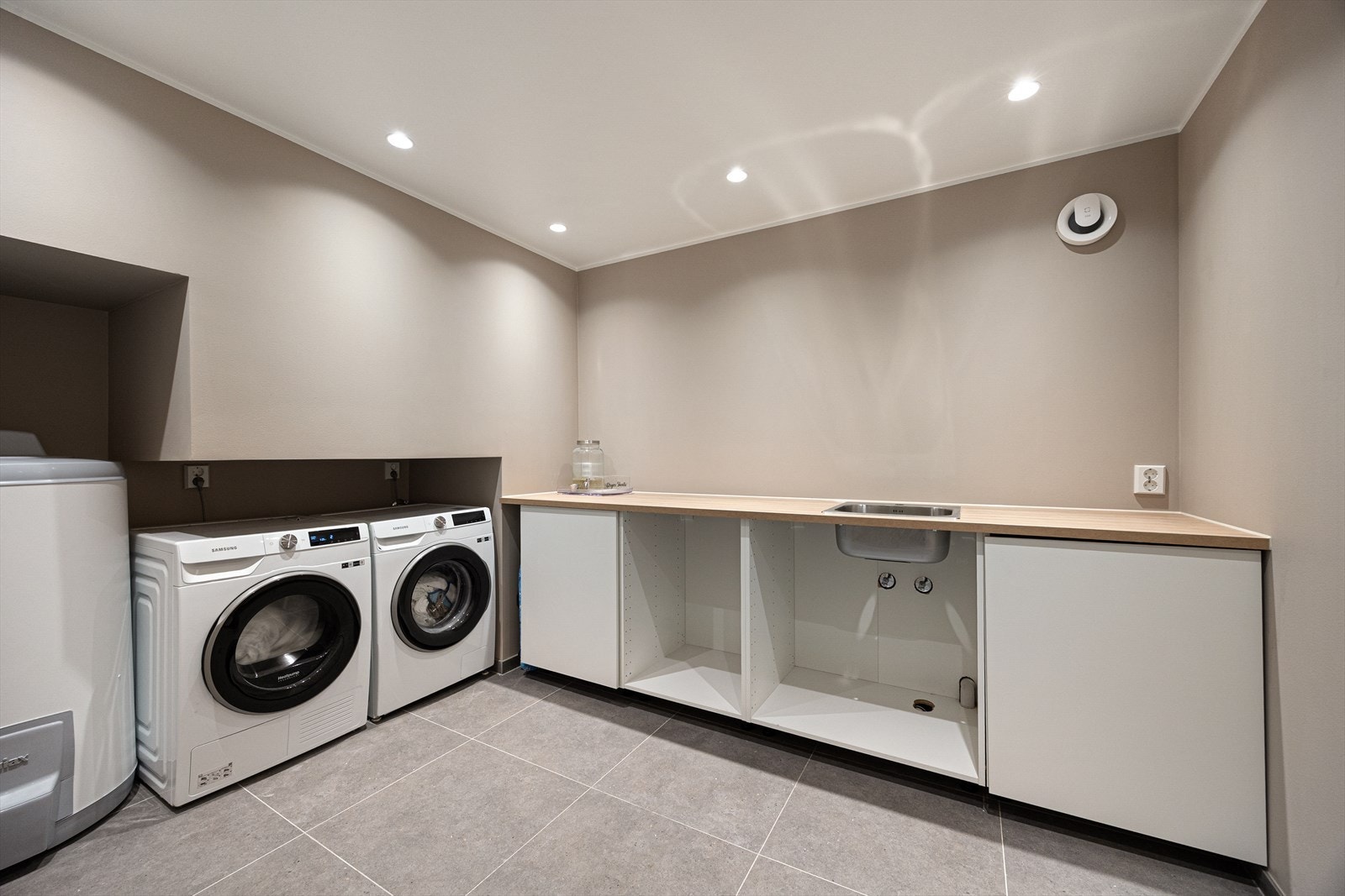 Praktisk vaskerom med flislagt gulv og sokkelflis langs veggene, tilrettelagt med opplegg for vaskemaskin og skyllekar. Galleribilde