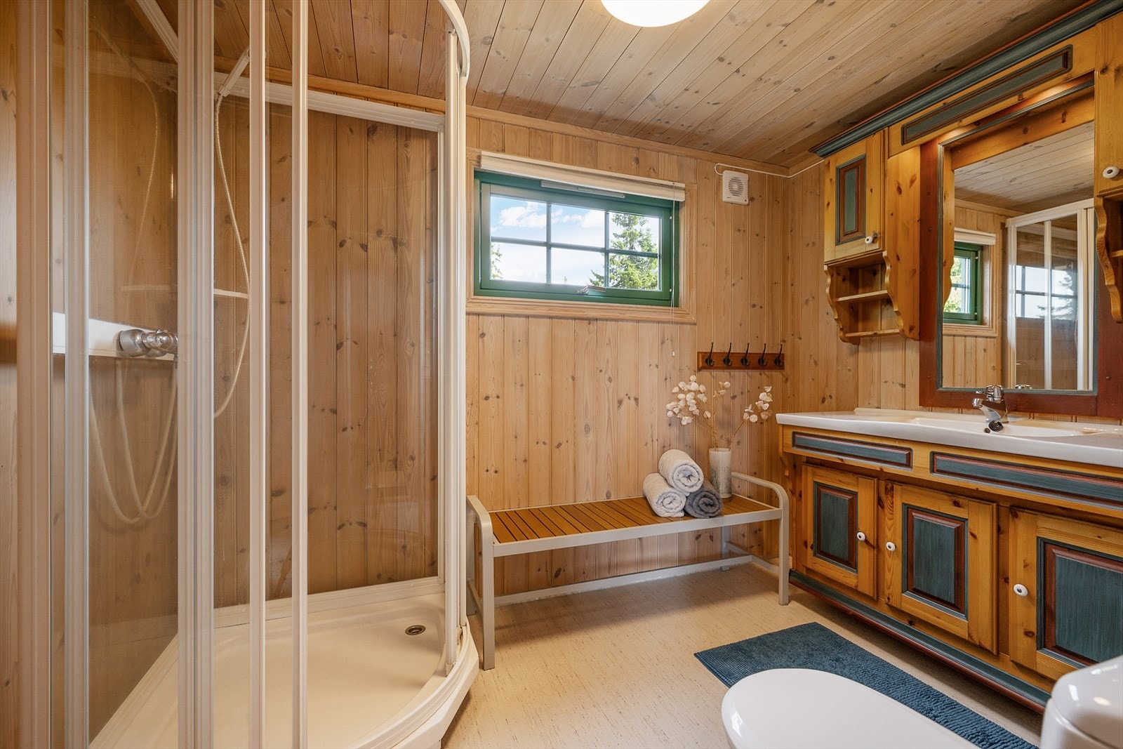 Praktisk bad/wc har dusjkabinett, romslig baderomsinnredning og gulvmontert wc. Panelte tak og vegger. Belegg på gulv. Galleribilde