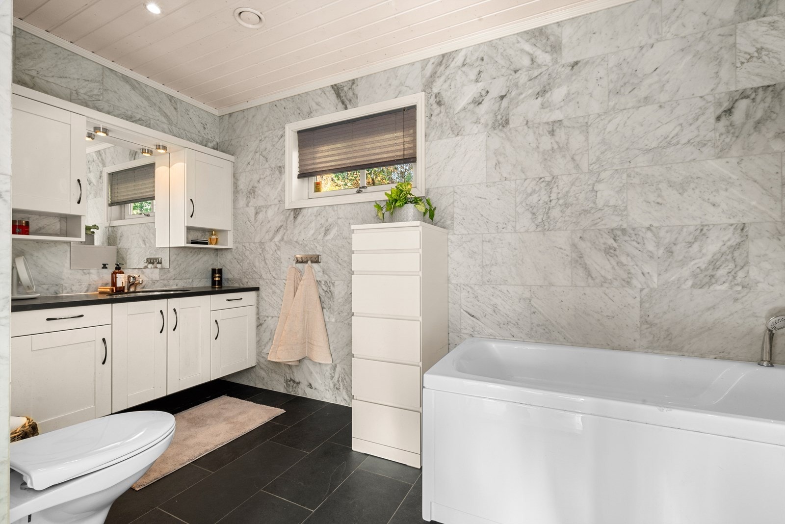 Boligen har to bad. Badet i 1. etasje er romslige 8 m² og er utstyrt med dusjhjørne, badekar, veggmontert toalett, servant i skap og elektrisk gulvvarme som gir ekstra komfort. Galleribilde