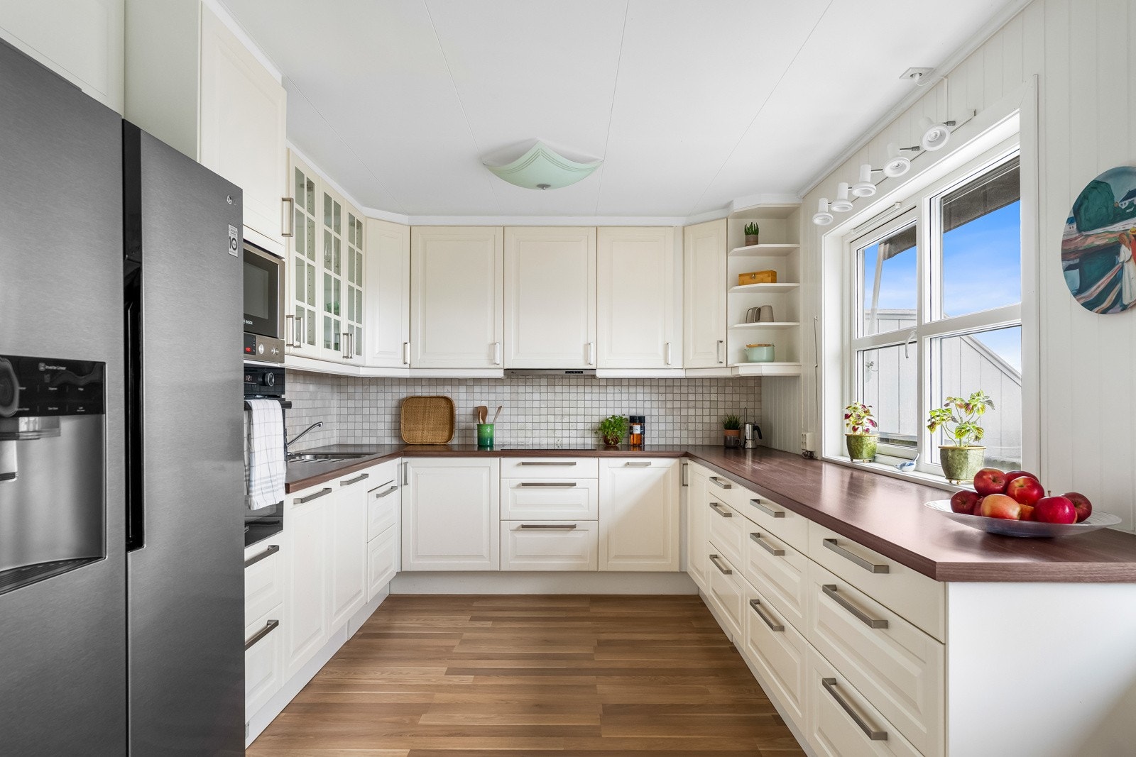 IKEA kjøkkeninnredning fra 2011. Enkelte glassfronter i overskap. Laminat benkeplate med planlimt kum i rustfritt stål. Ventilator. Stekeovn, keramisk topp og oppvaskmaskin. Frittstående kjøl/frys. Fliser på vegg over benkeskap. Galleribilde