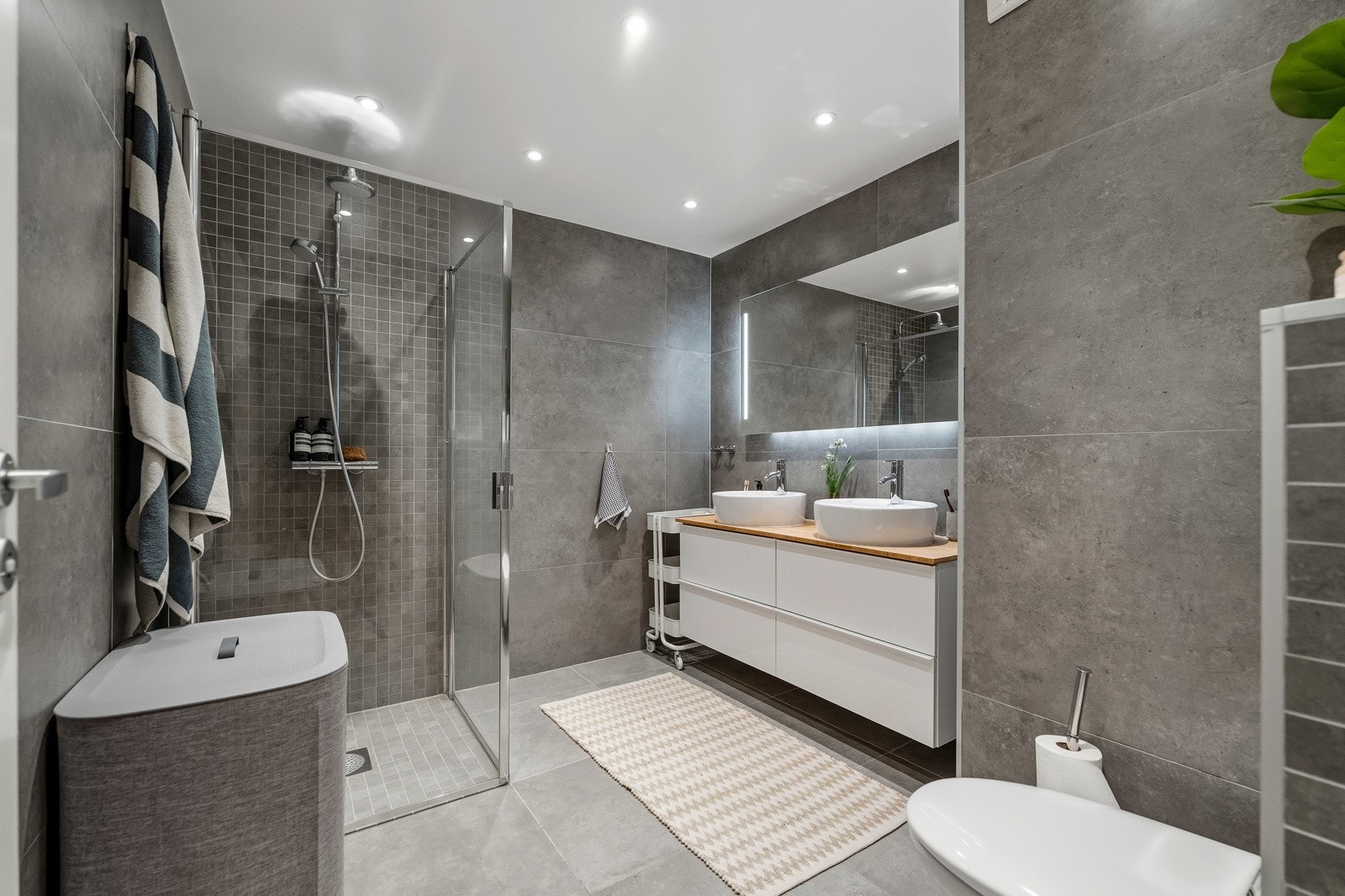 Badet i 2. etasje er fra ca. 2018 og har dusjdører i glass, dobbel servant, speil med belysning, vegghengt toalett og downlights. Begge fremstår stilfulle, funksjonelle og solid. Galleribilde