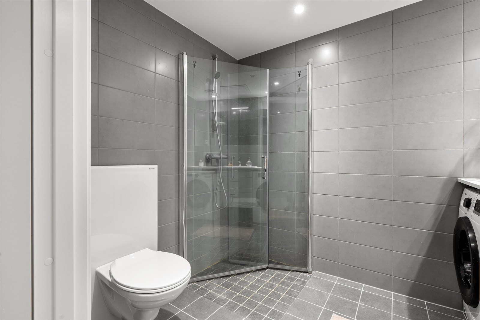 Badet har et veggmontert toalett og et praktisk dusjhjørne med innfellbare dører. Galleribilde