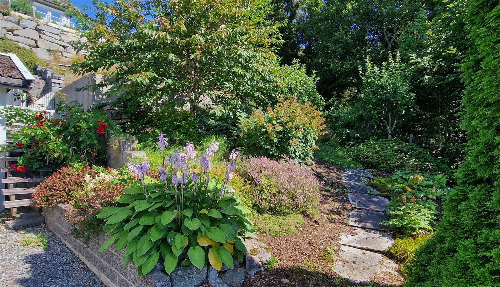 Pent opparbeidd uteområde med naturstein og beplantning som gir eit skjerma og innbydande preg. (Selgers eige bilete) Galleribilde