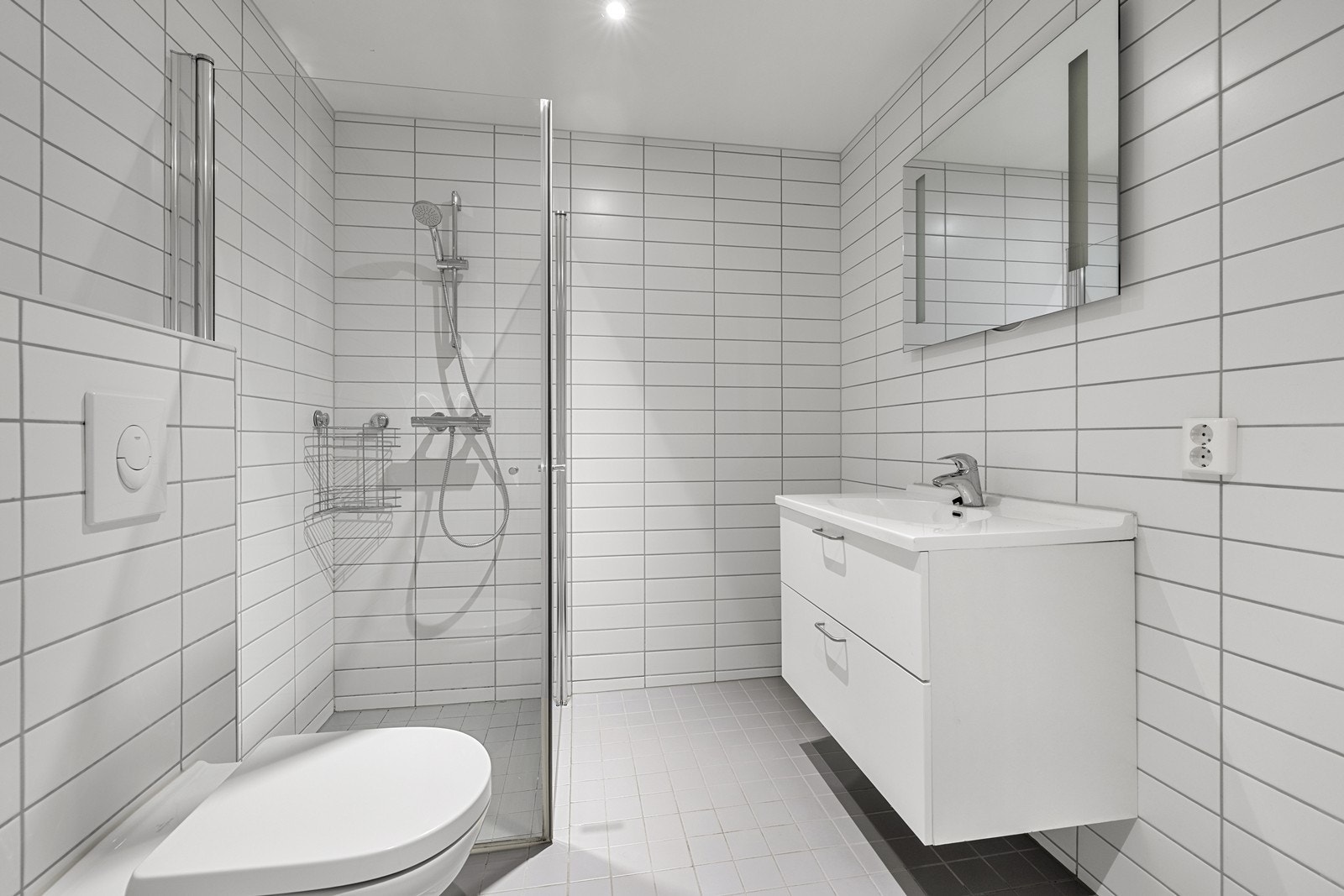 Badet er innredet med veggmontert toalett, dusjhjørne, heldekkende servant og opplegg for vaskemaskin. Galleribilde