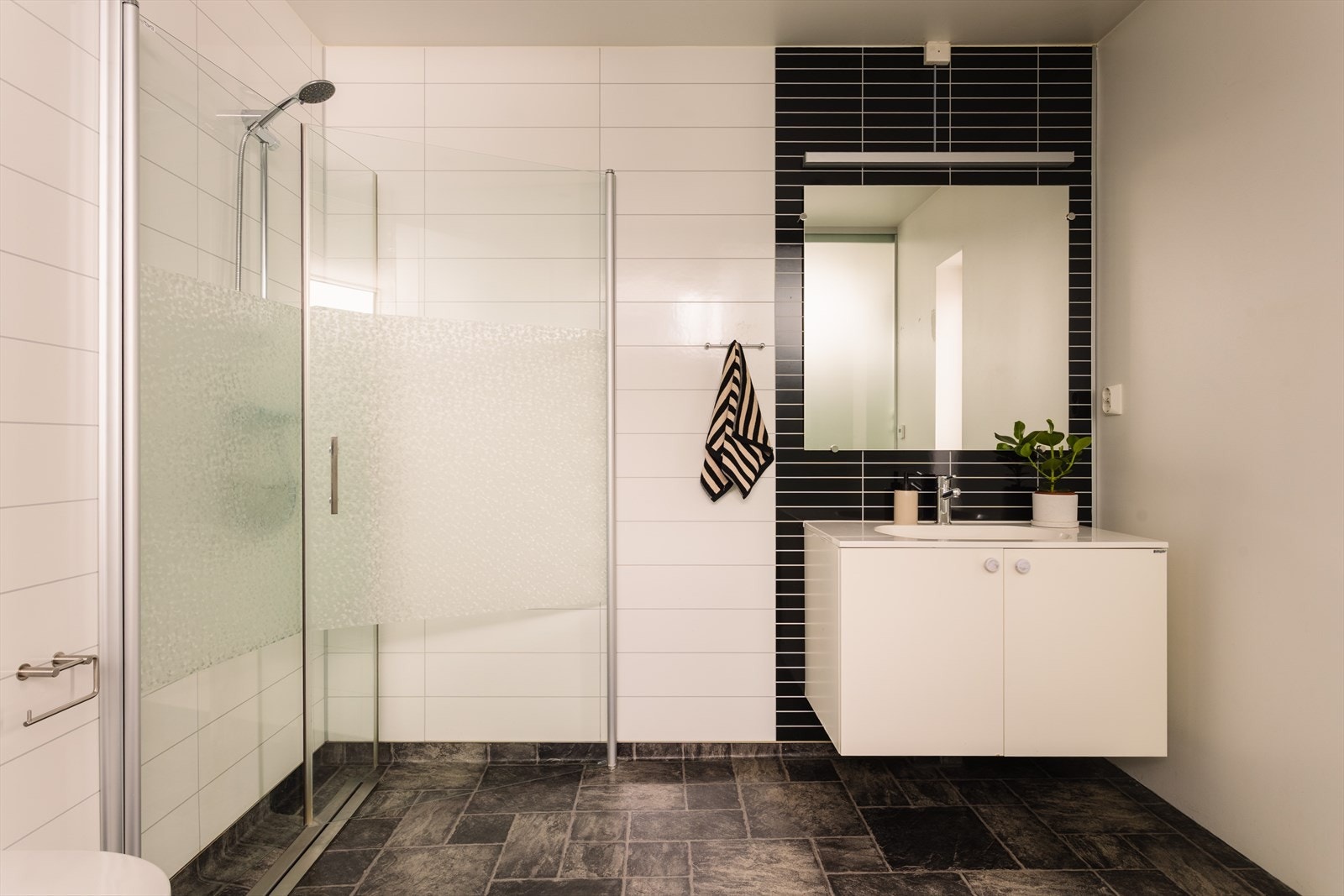 Tidløst og delikat baderom med vegghengt toalett, dusjhjørne med innfellbare glassdører og vegghengt servantinnredning. Galleribilde