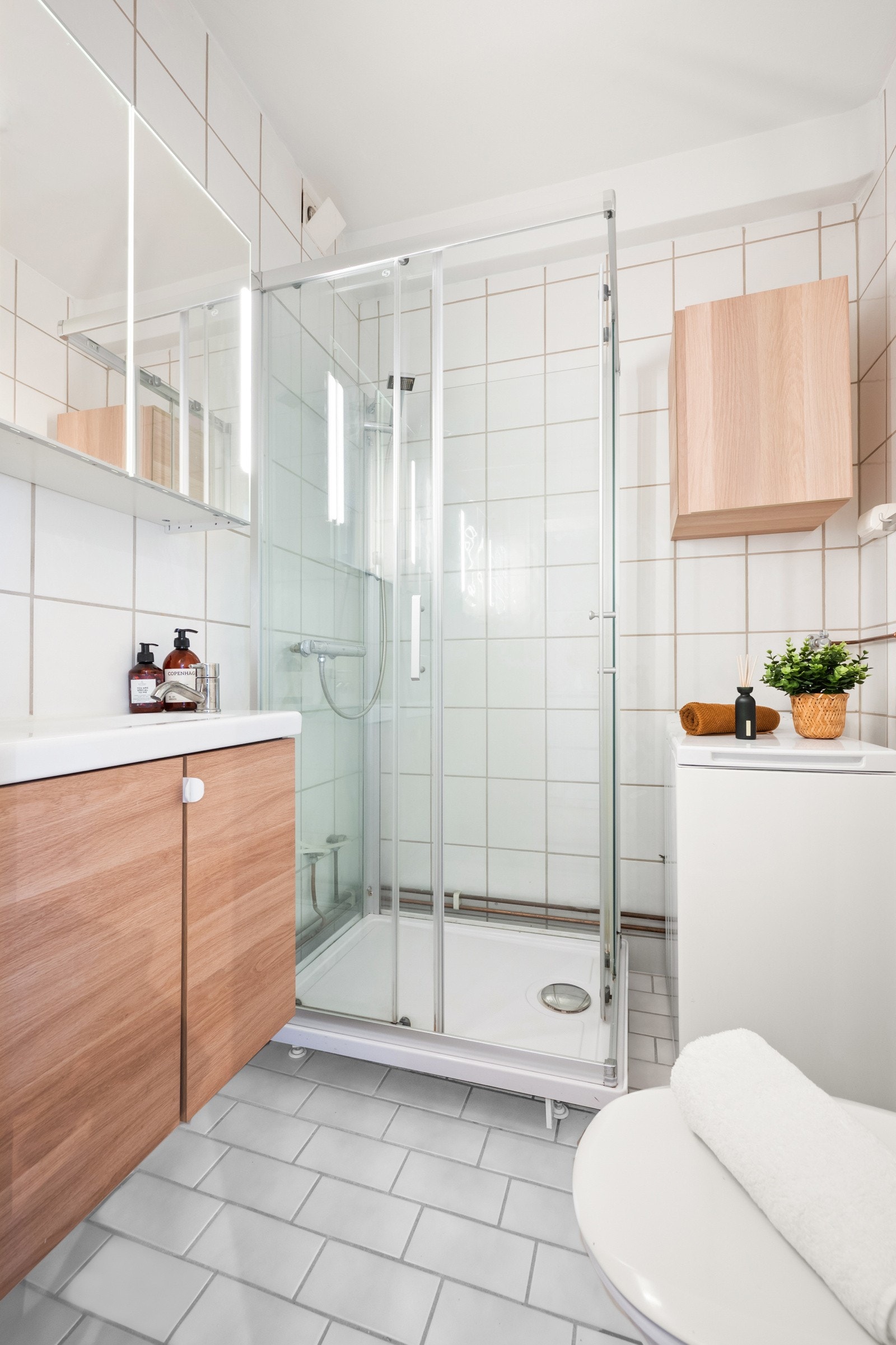 Baderom med gulvstående toalett, dusjkabinett, servant med slette fronter og opplegg for vaskemaskin. Ukjent alder på badet, med nyere innredning fra IKEA i 2019. Badet har naturlig ventilasjon. Tak malt i 2025. Galleribilde