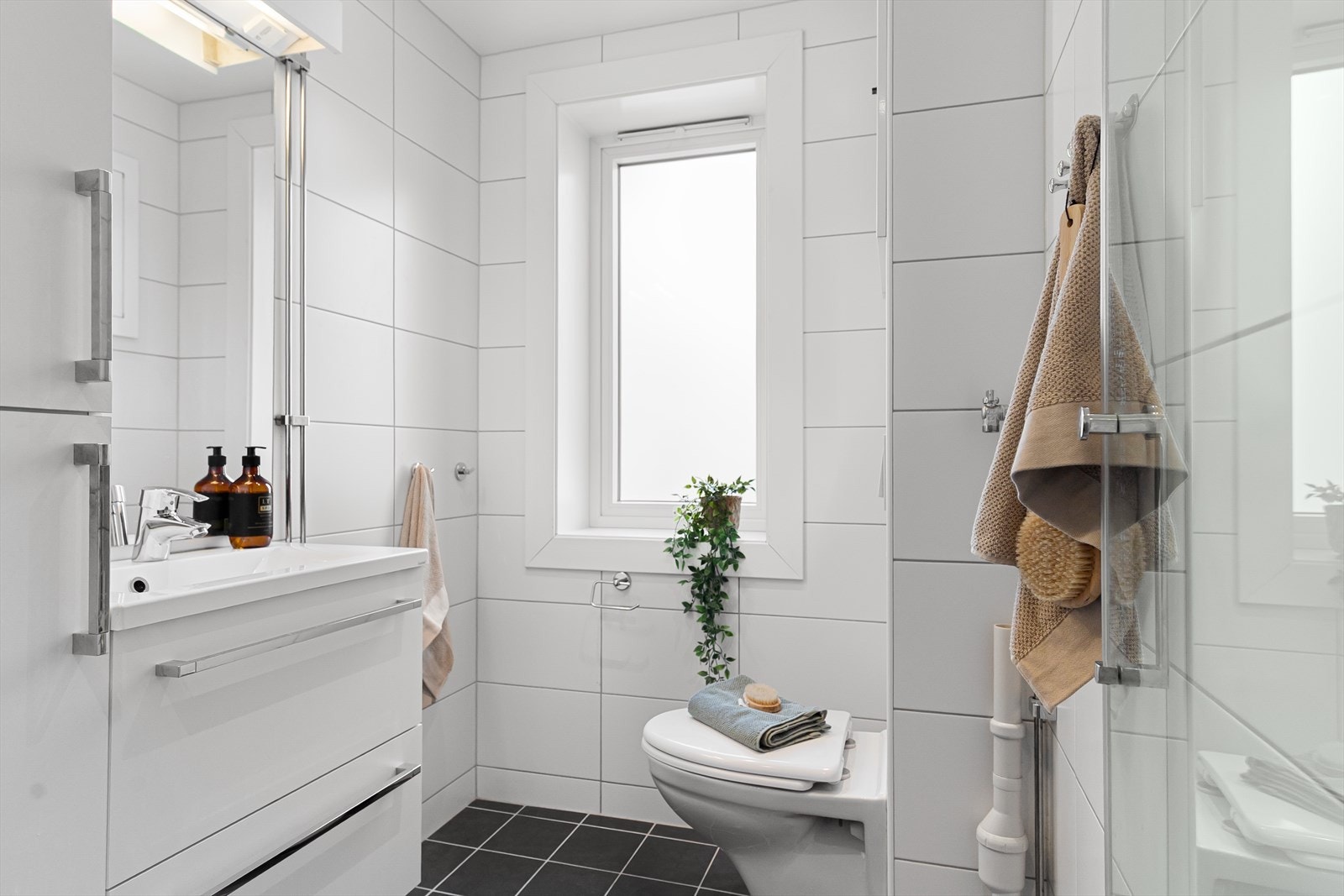 Badet er pent innredet med servant med underskap og skap med hvite fronter, over servanten er det speil med lampe og enkel stikkontakt. Galleribilde