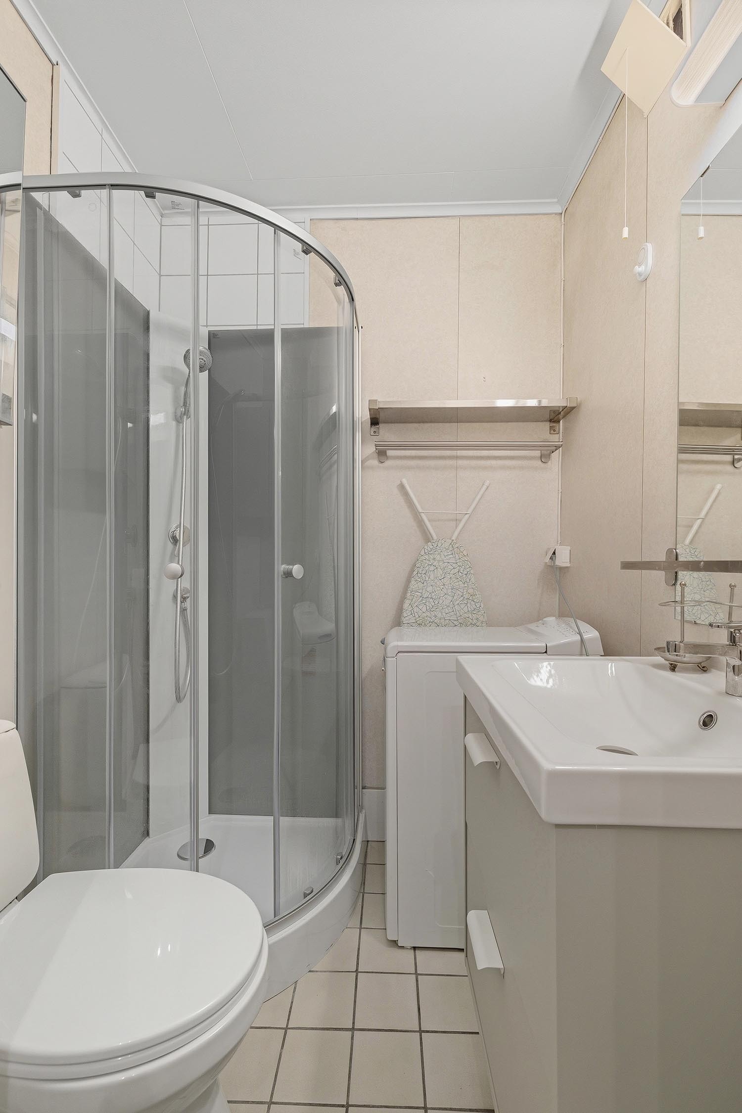 Pent flislagt bad med toalett vaskemaskin, servant og hjørnedusj. Galleribilde