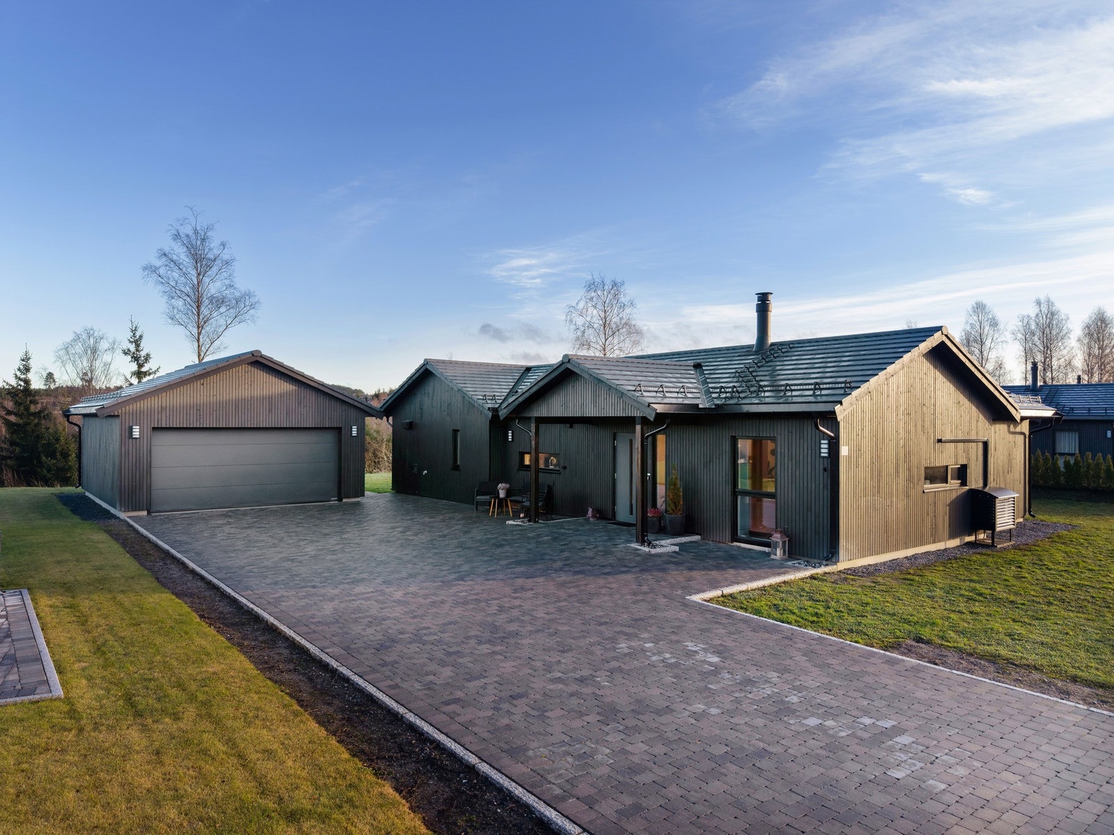 Flott opparbeidelse av tomten med stor steinlagt gårdsplass og flate plenarealer Galleribilde