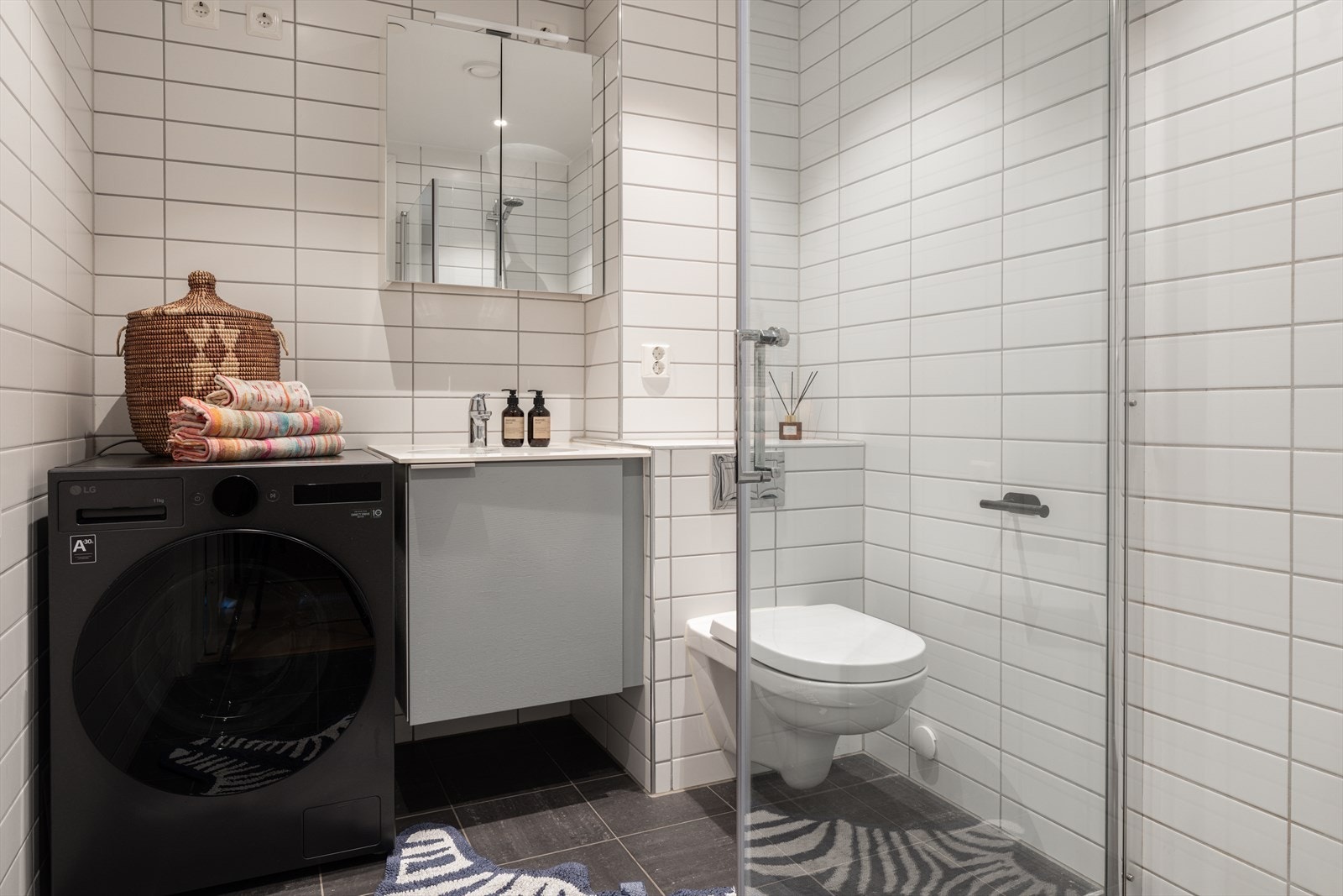 Lekkert flislagt baderom med gulvvarme og opplegg for vaskemaskin Galleribilde