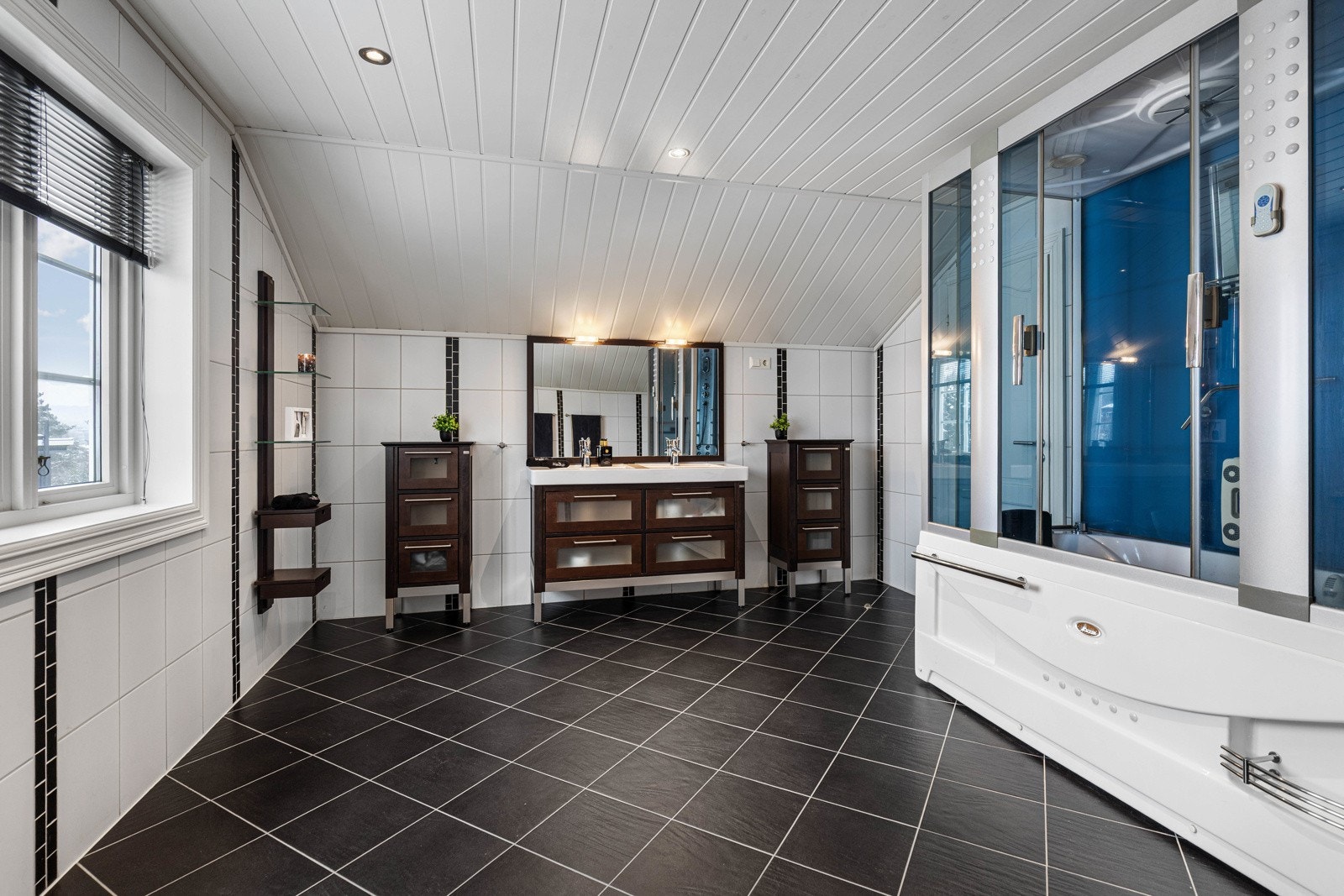 Badet er stilrent innredet med stort dusjkabinett, toalett, Duo dobbel servant med underskuffer, stort speil og vegghengte hyller - alt i en gjennomført og klassisk stil. Galleribilde