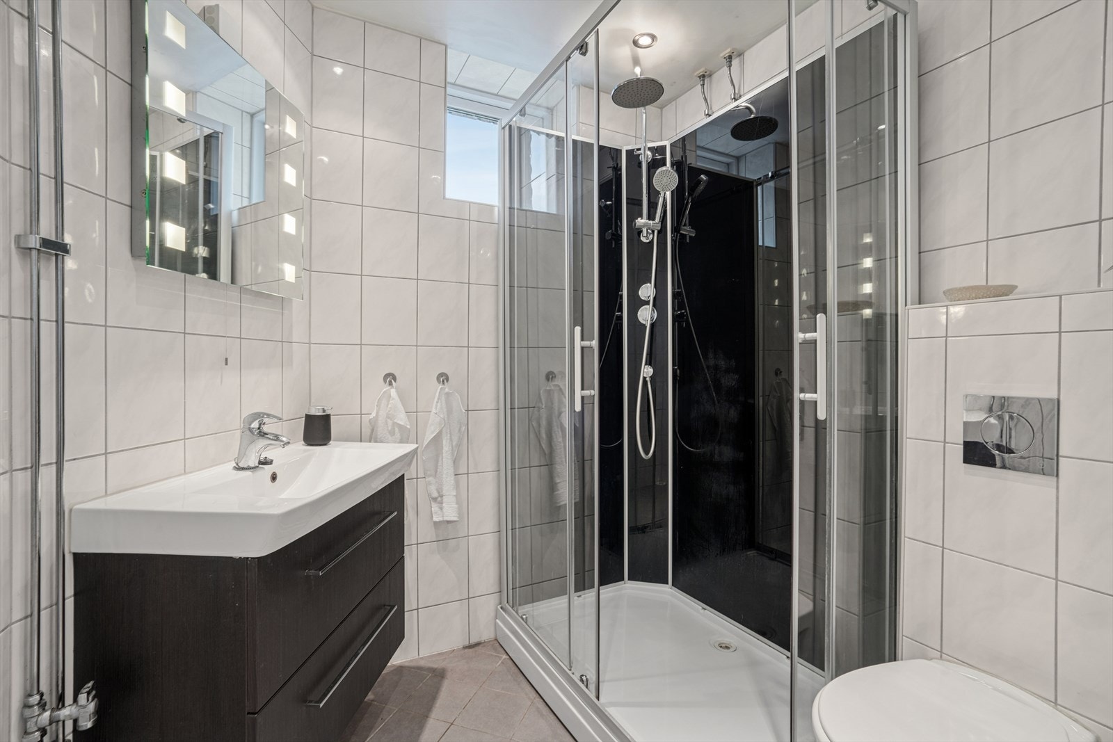 Badet er innredet med servantskap med ett-greps blandebatteri, speil med lys, vegghengt toalett med innebygget sisterne og dusjkabinett. Galleribilde