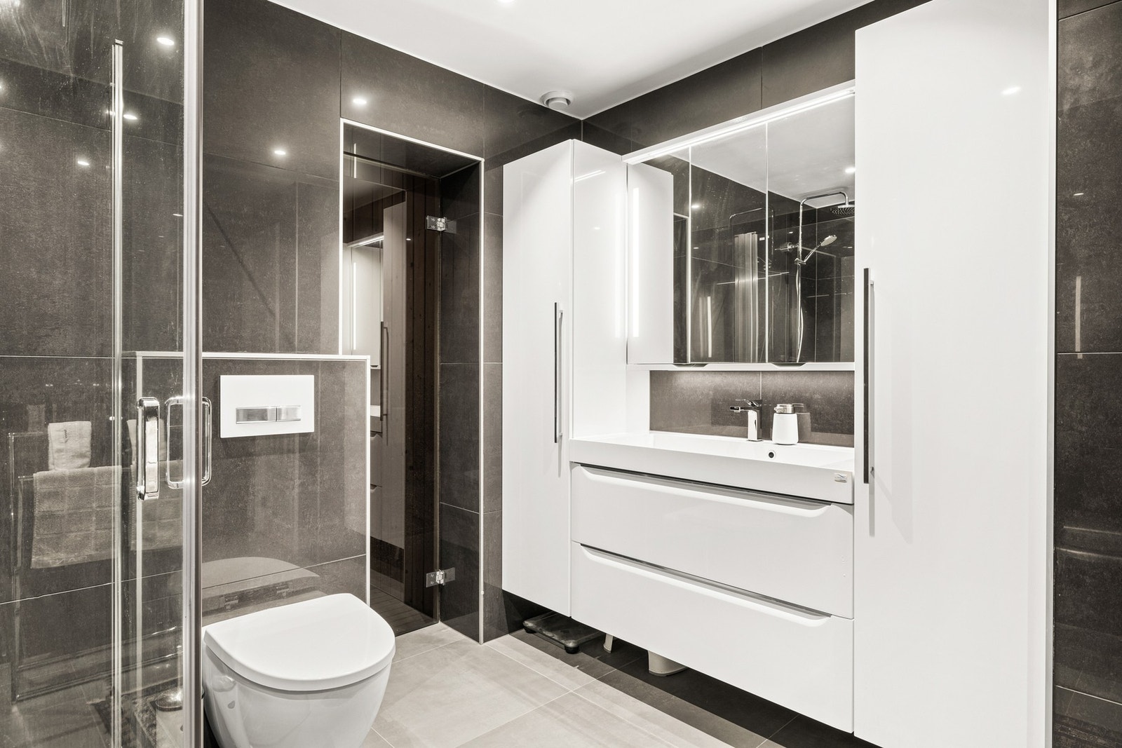 Alle vegger er flislagt fra gulv til tak med mørke, elegante fliser som gir rommet et eksklusivt uttrykk. Galleribilde