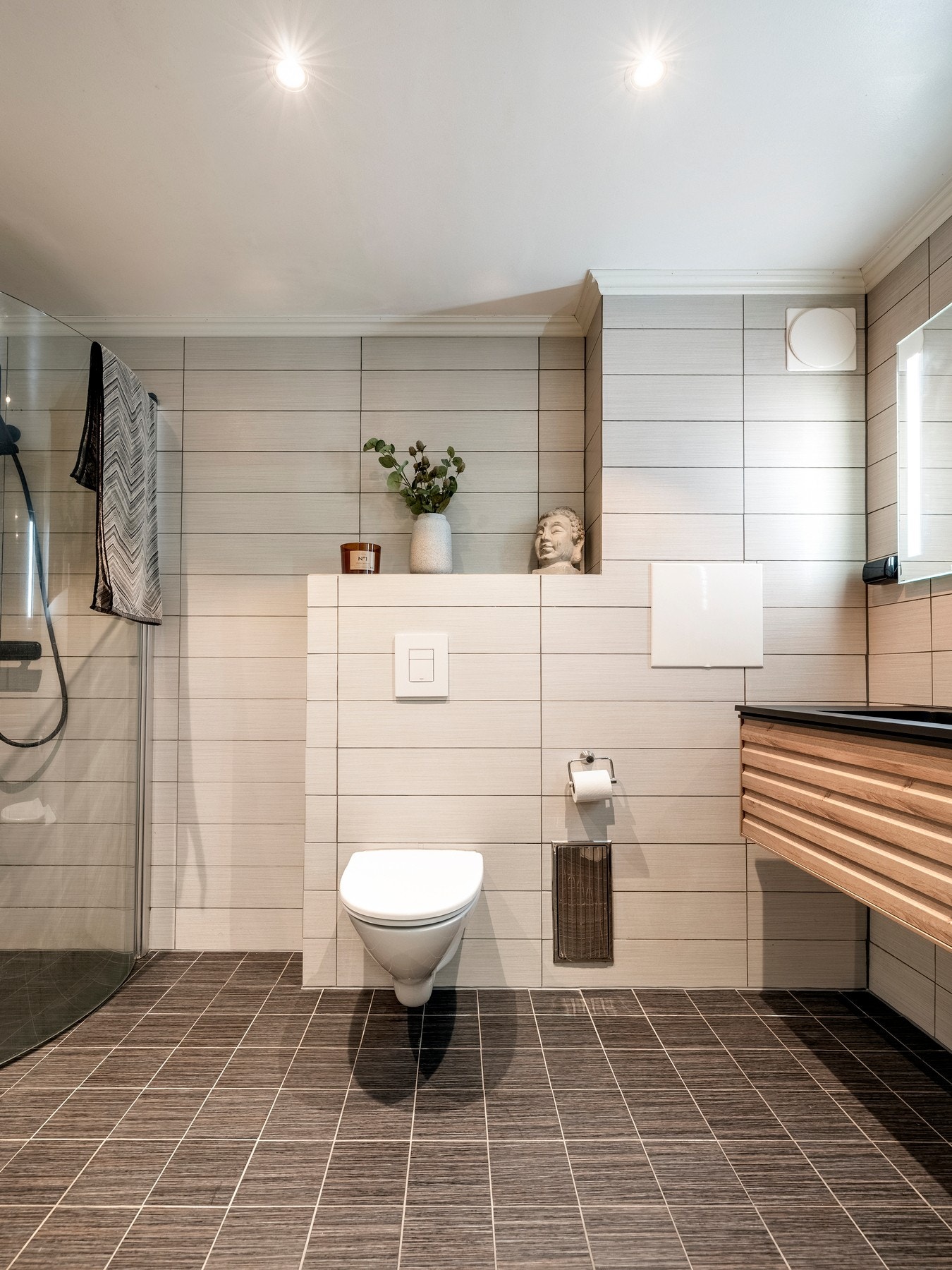 Rommet er innredet med servantinnredning, speil med lys på vegg over servant, vegghengt toalett og dusjhjørne med svingbare glassdører. Galleribilde