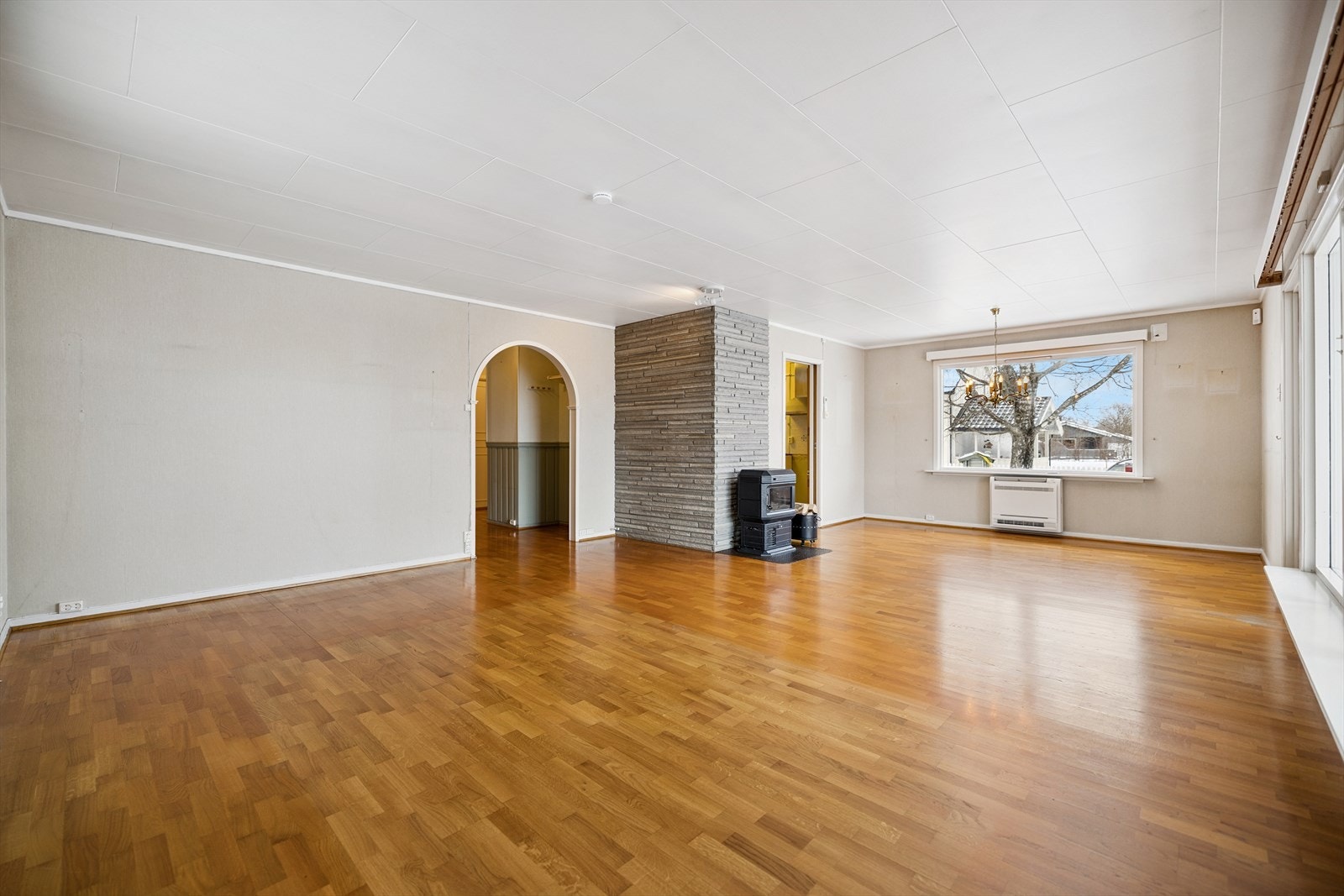 Romslig stue med parkett på gulv og store vindusflater. Vedovn som supplerende varmekilde. Galleribilde