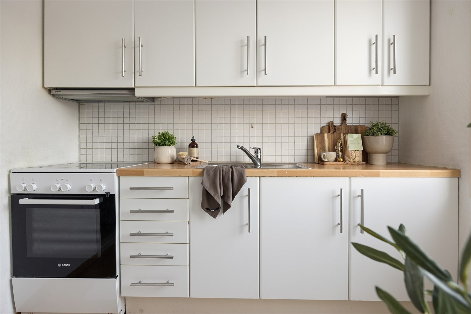 Integrerte hvitevarer og flislagt vegg over benkeplate gir en funksjonell arbeidsplass på kjøkkenet. Galleribilde