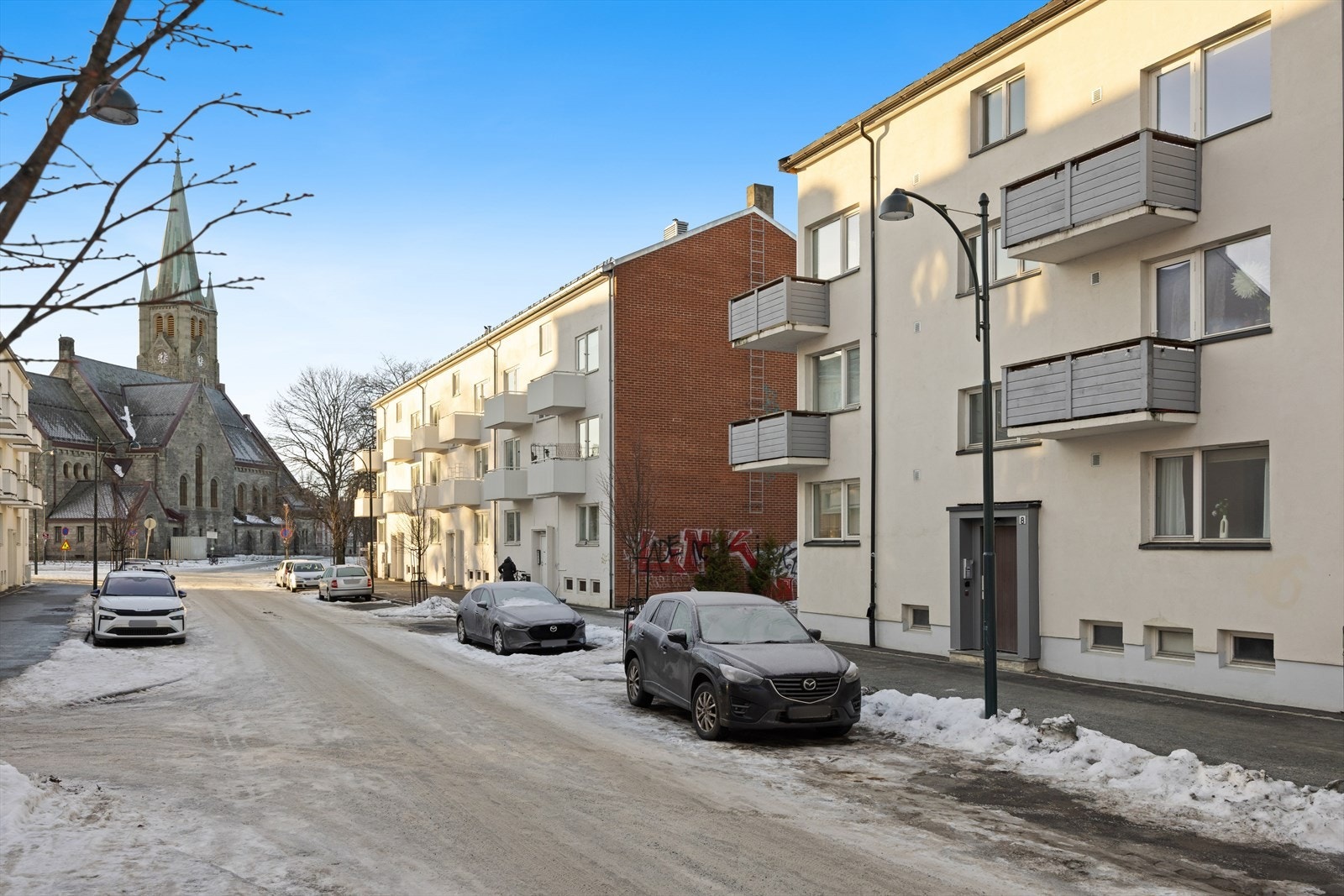Gatebilde med leilighetsbygg og kirke i bakgrunnen viser en rolig og attraktiv beliggenhet. Galleribilde