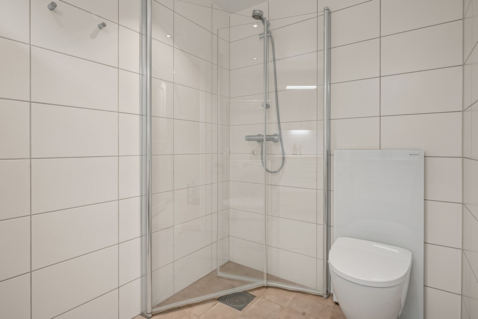 Videre er badet utstyrt med veggmontert klosett med utvendig sisterne samt dusjhjørne med rette svingdører. Galleribilde