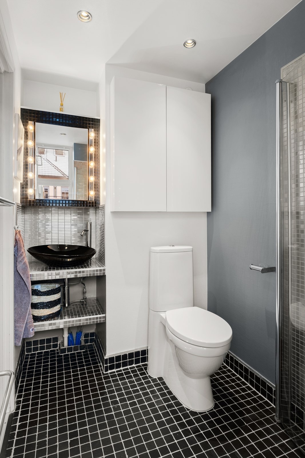 Innredningen består av servant, vegghengt skap, gulvmontert toalett og dusjhjørne med stilrene svingdører i glass. Galleribilde