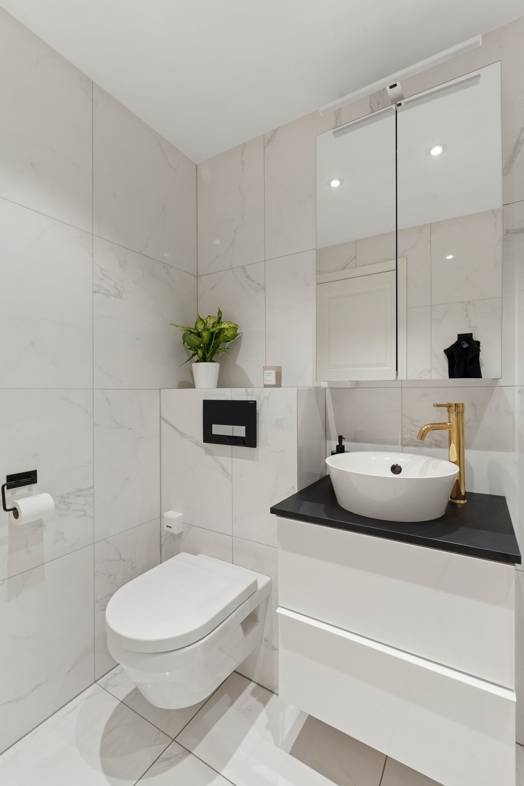 Badet er utstyrt med dusjhjørne med fast felt i herdet glass, servantsinnredning med veggfestet klosett med innebygget sisterne. Galleribilde