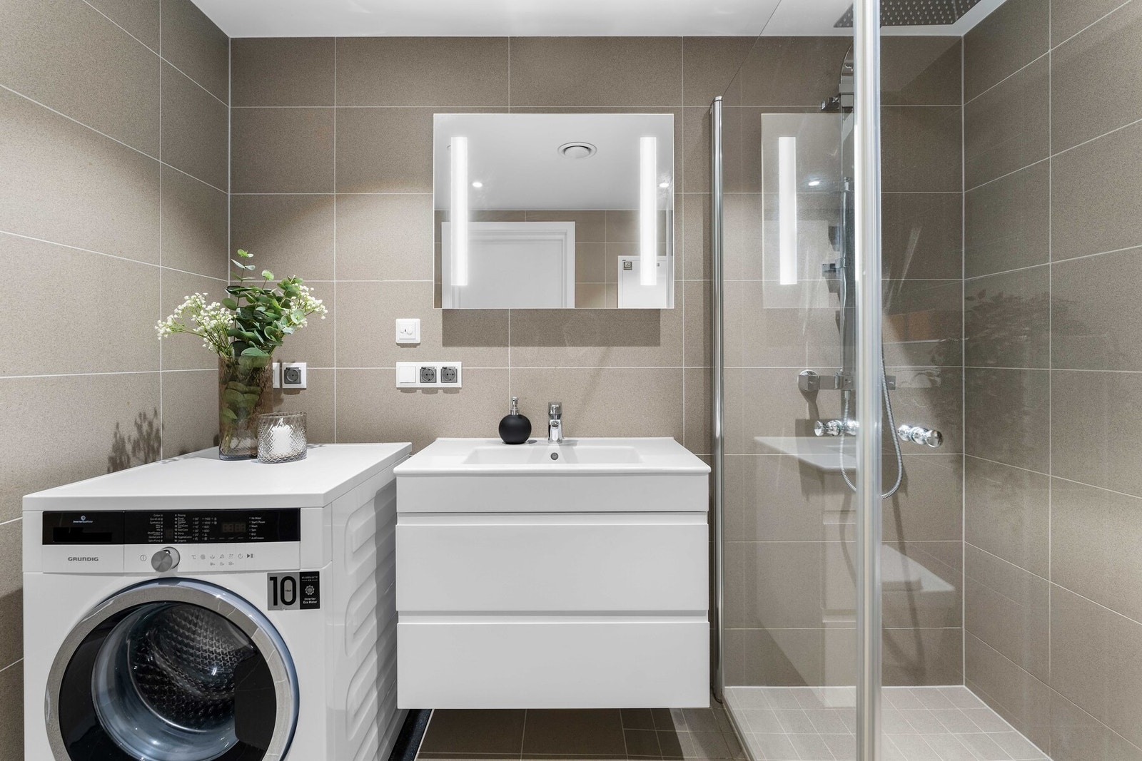 Delikat bad med flislagte overflater og vannbåren gulvvarme. Baderomsinnredningen består av moderne servantmøblement med heldekkende hvit blank vask og speil med integrert LED lys. Videre er det vegghengt toalett og dusjhjørne. Galleribilde