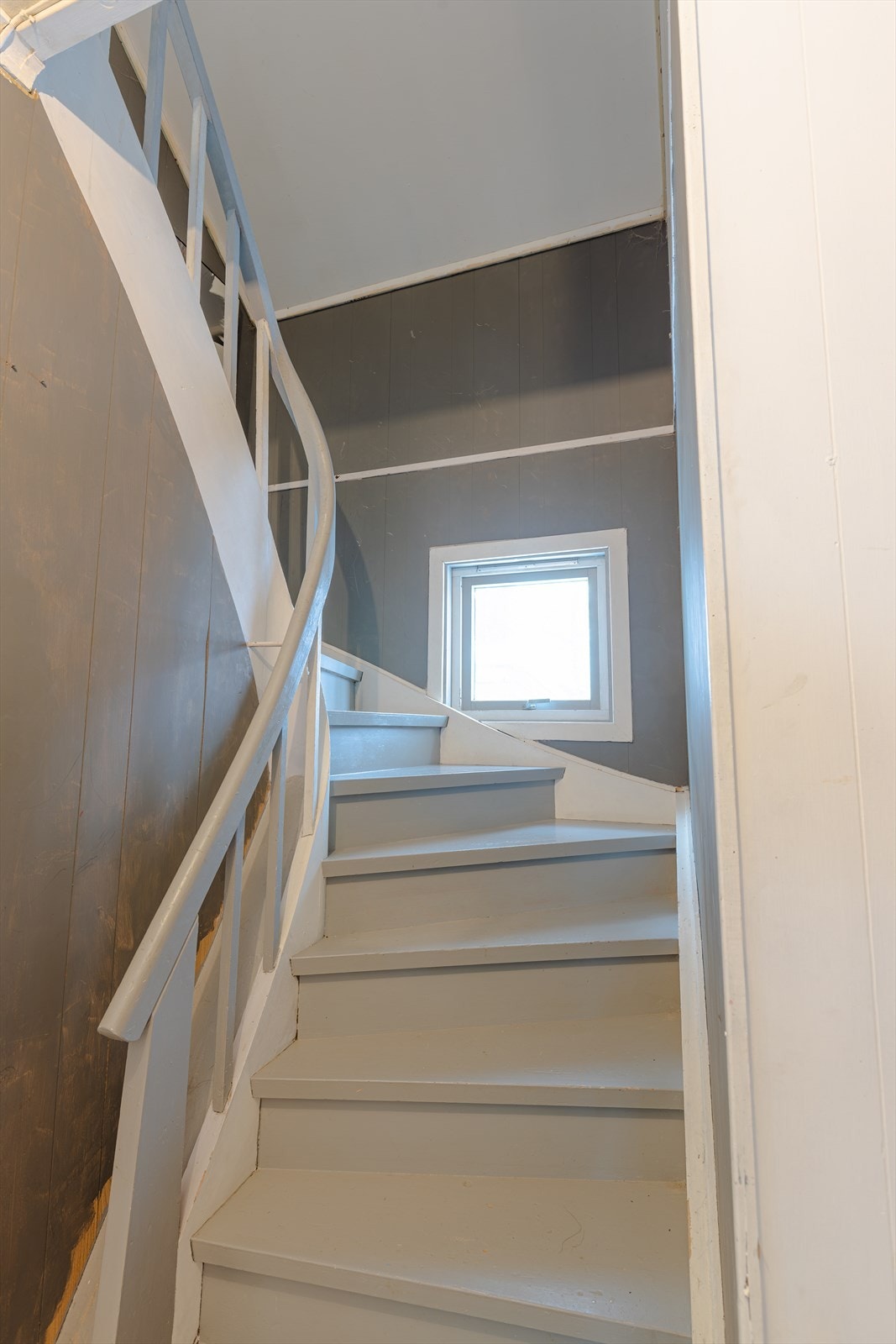 Malt tretrapp gir tilgang mellom etasjene i boligen, med et vindu som slipper inn naturlig lys. Galleribilde