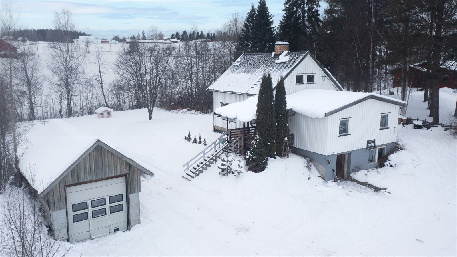 Luftfoto av eiendommen viser eneboligen med tilhørende garasje og snødekte omgivelser. Galleribilde