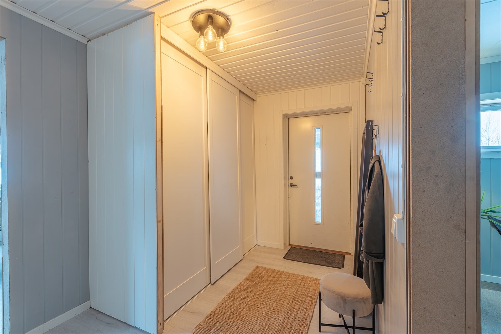 Skyvedørsgarderobe gir effektiv oppbevaring i entréen. Panelvegger og tak med himlingsplater skaper et helhetlig uttrykk. Galleribilde