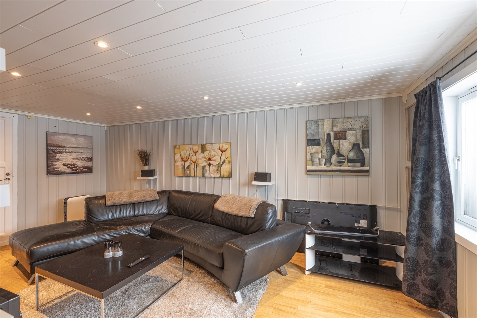 Kjellerstue med laminatgulv og panelvegger gir en moderne finish til stuen, som også har en peisovn for ekstra varme. Galleribilde