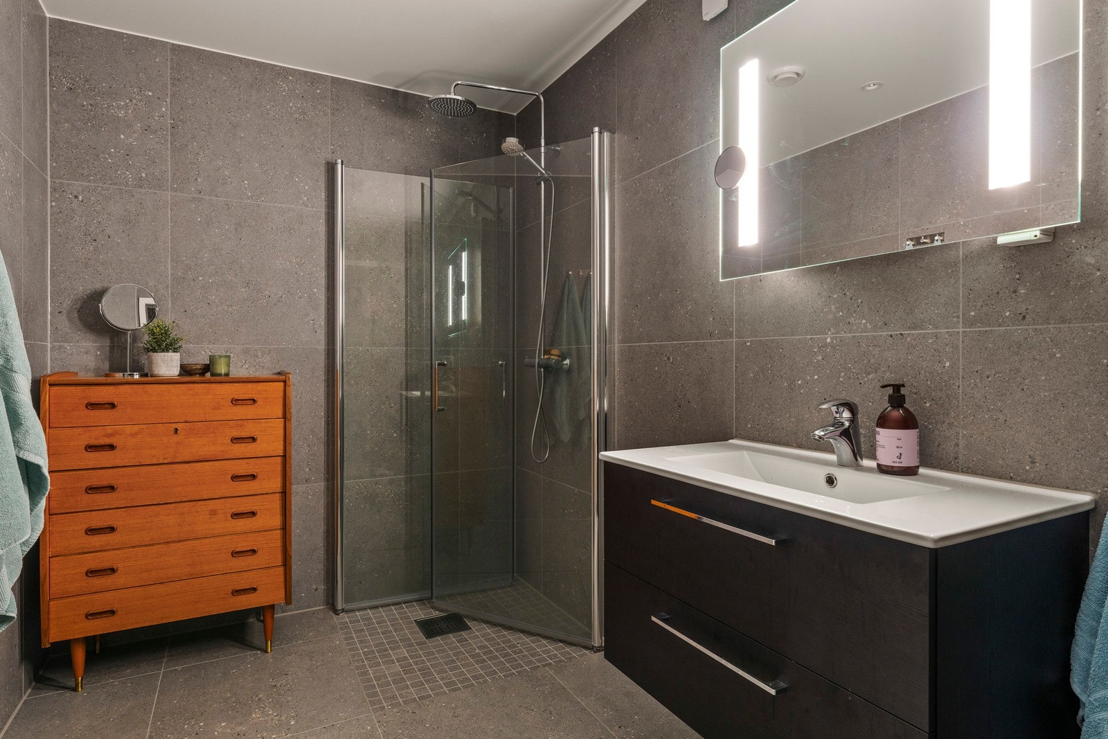 Badet er utstyrt med dusj med innfellbare dører i herdet glass, vegghengt vask og vegghengt toalett. Galleribilde