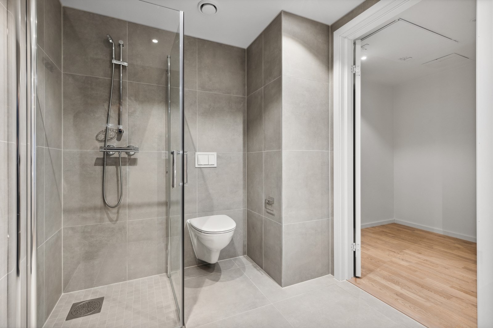 Delikat, flislagt bad med vegghengt toalett og dusjhjørne med svingbare glassdører. Galleribilde