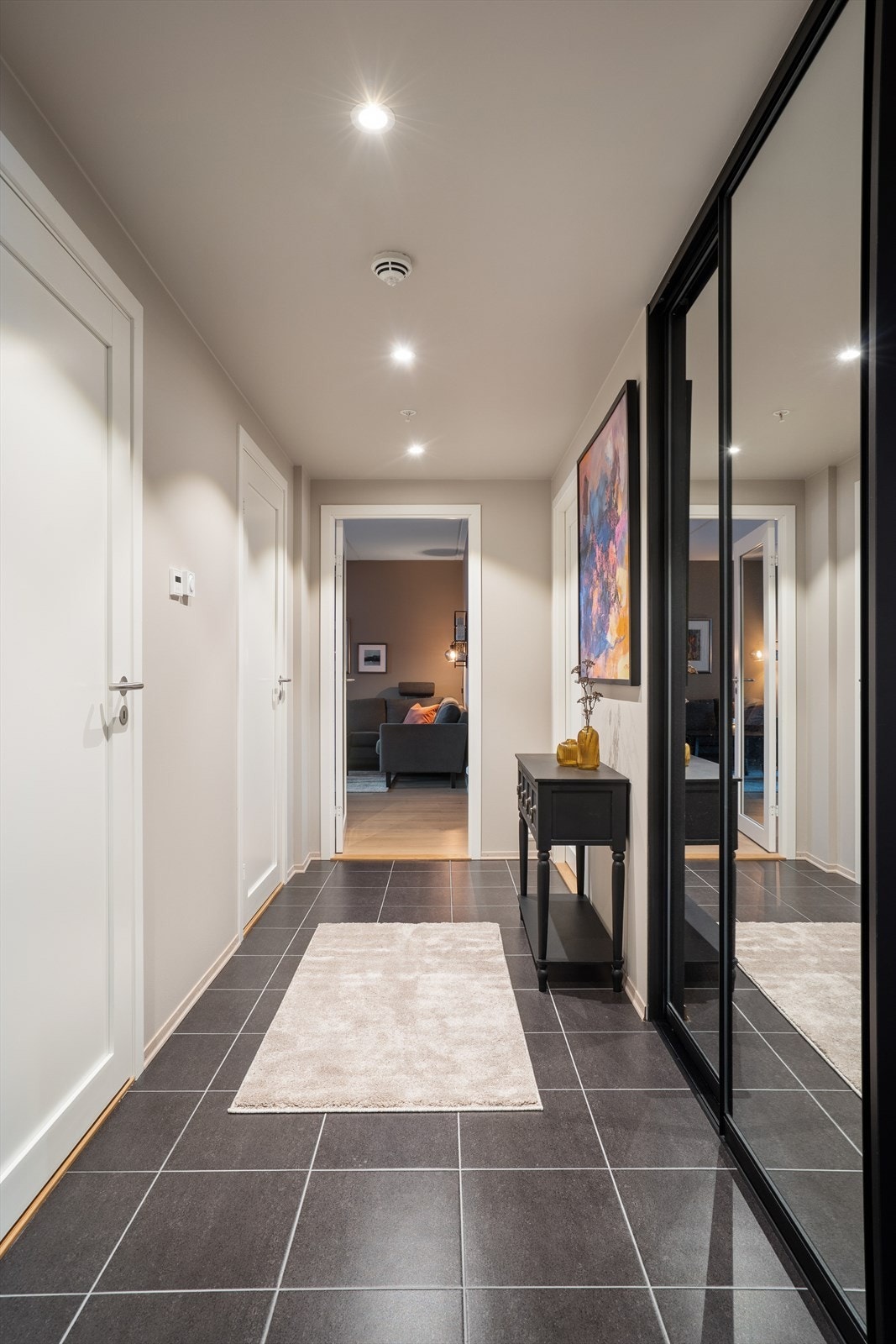 Man ønskes velkommen inn i en stor gang som er praktisk innredet med flislagt gulv og en stor skyvedørsgarderobe hvor man har god plass til å henge fra seg yttertøy og sko. Her får man umiddelbart et godt førsteinntrykk av leiligheten! Galleribilde