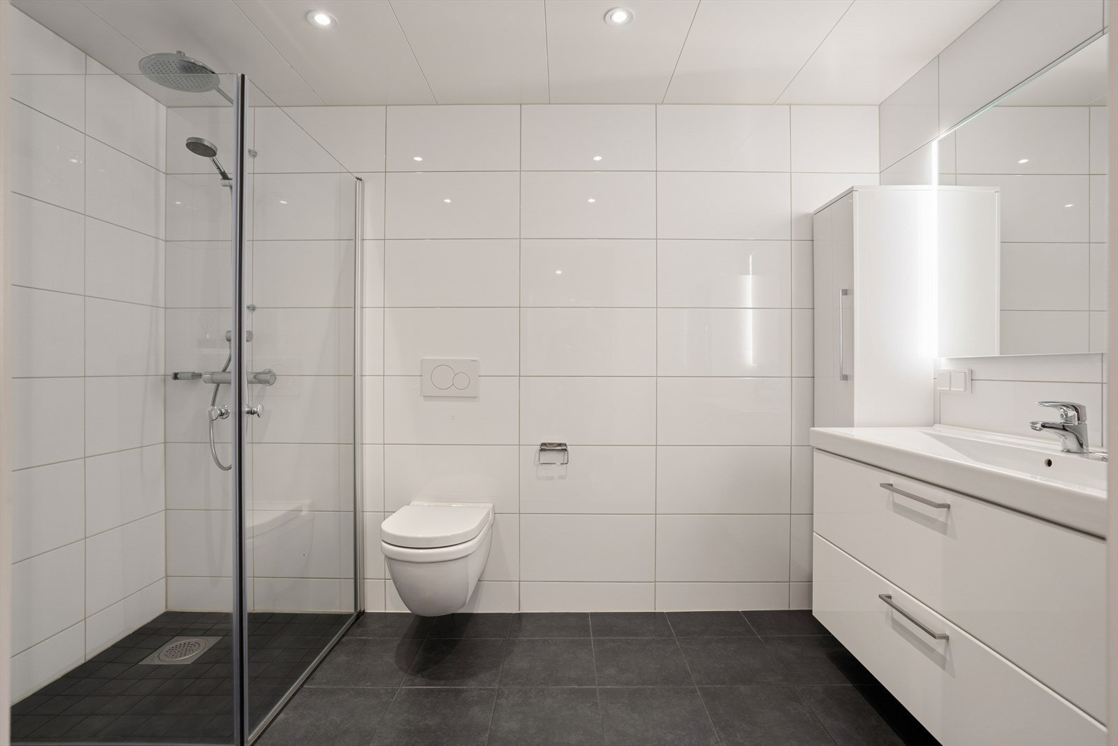 Badet er ellers utstyrt med dusjhjørne, vegghengt toalett og baderomsinnredning med nedfelt servant. Avtrekk via balansert ventilasjonsanlegg. Galleribilde