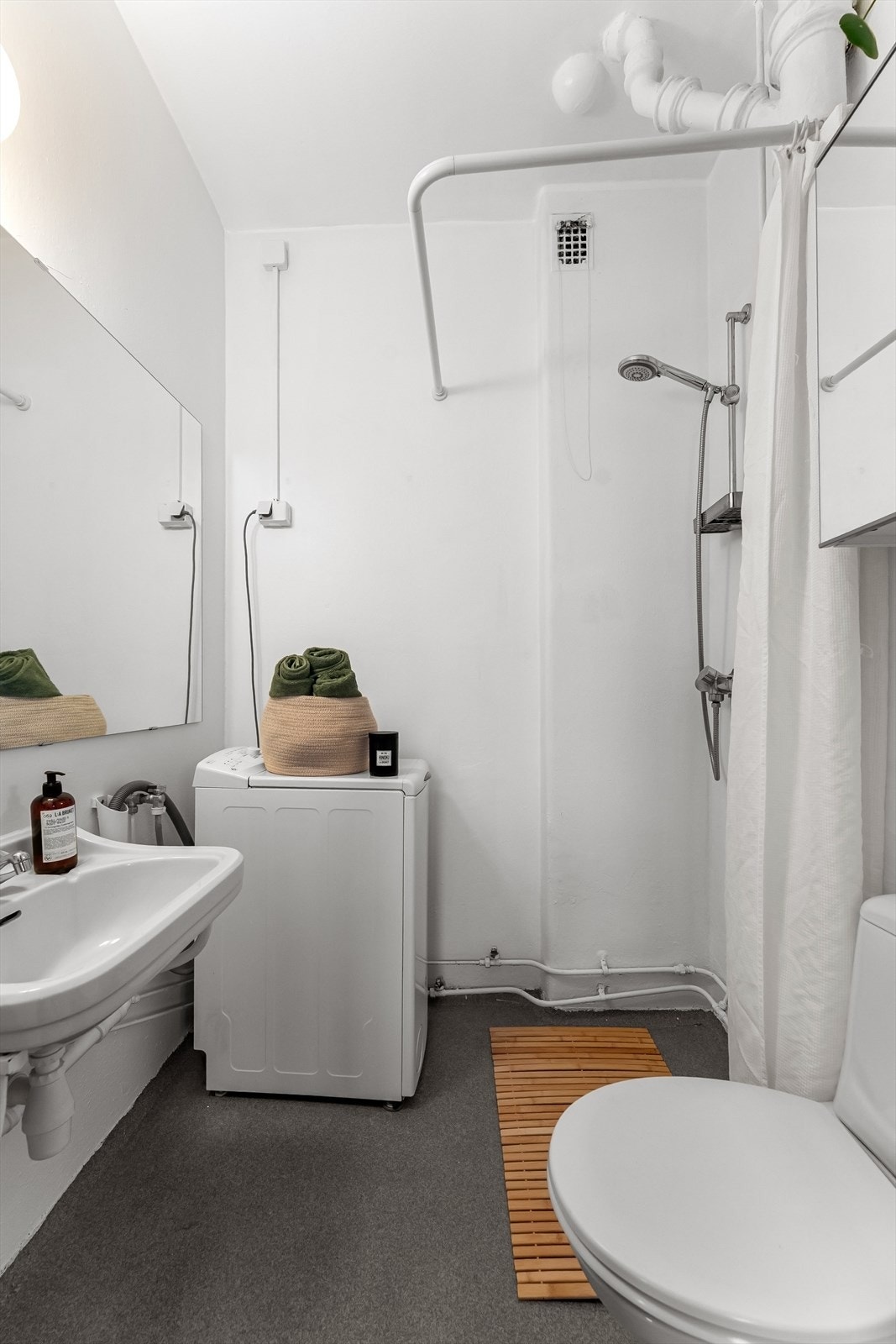 Eldre bad med dusj på gulv, servant gulvstående klosett og opplegg for vaskemaskin Galleribilde